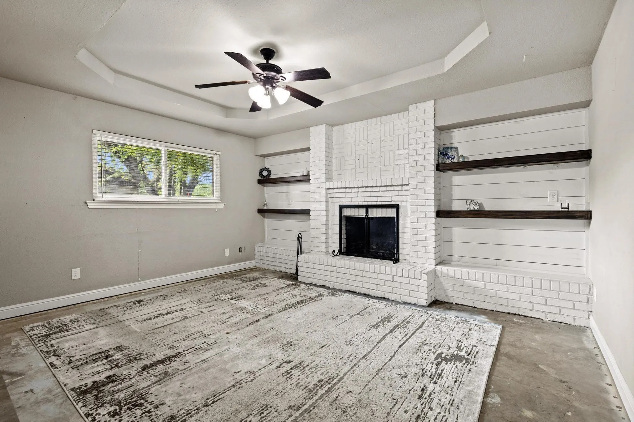 Living space featuring a white brick fireplace with a black iron screen, flanked by built-in shiplap shelving with dark wood-finish shelves. New carpet installed 08-12-2026.