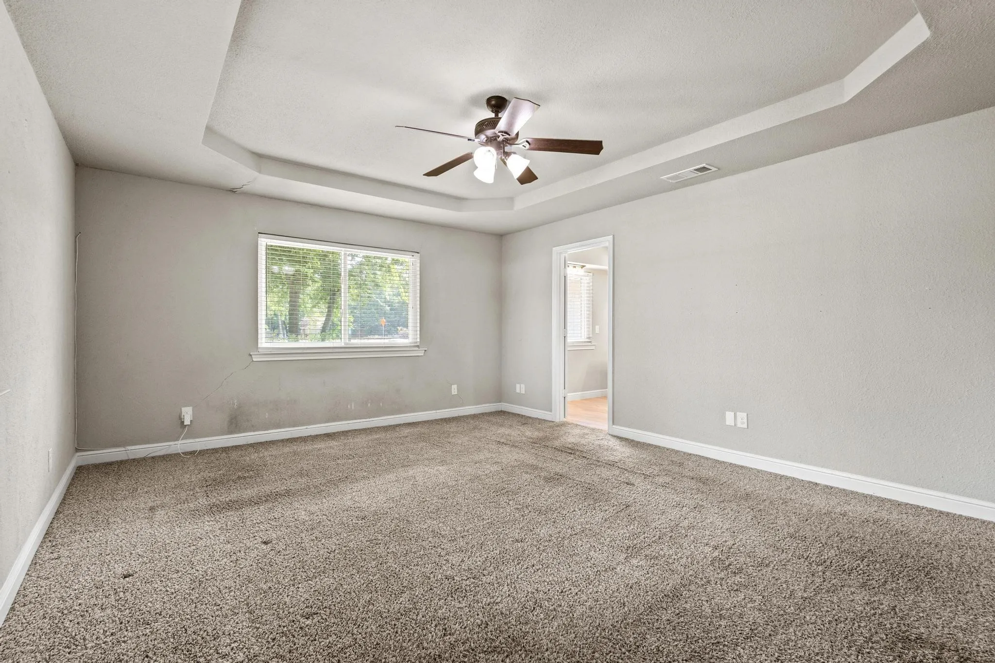 Spacious room featuring tray ceiling, ceiling fan, and carpeted flooring. Carpet replaced 08-12-2026.