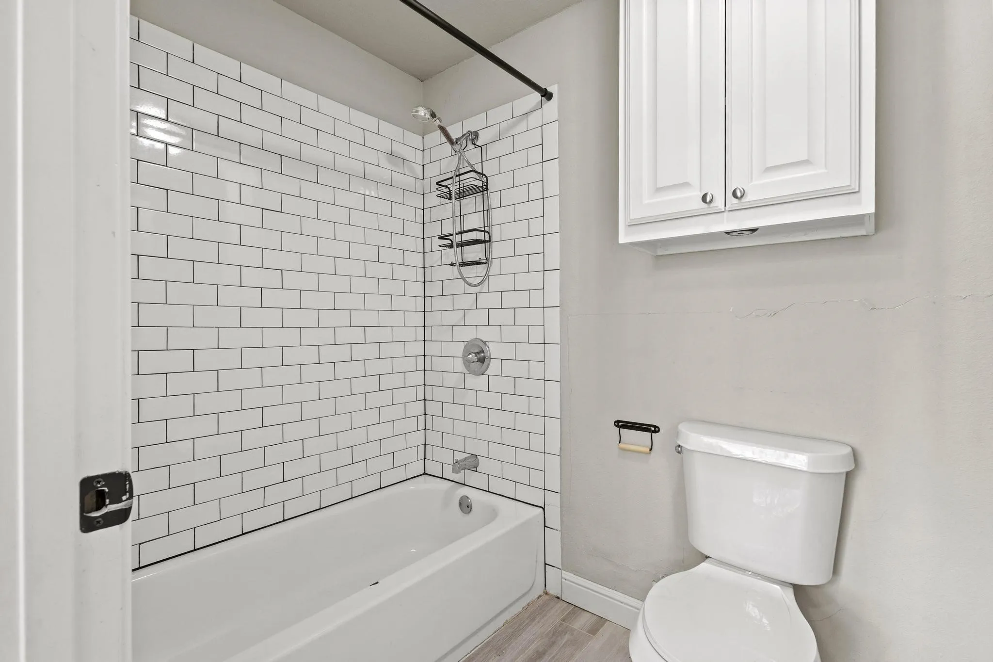 Bathroom featuring a white subway tile shower surround, a white bathtub, and wood-finish flooring