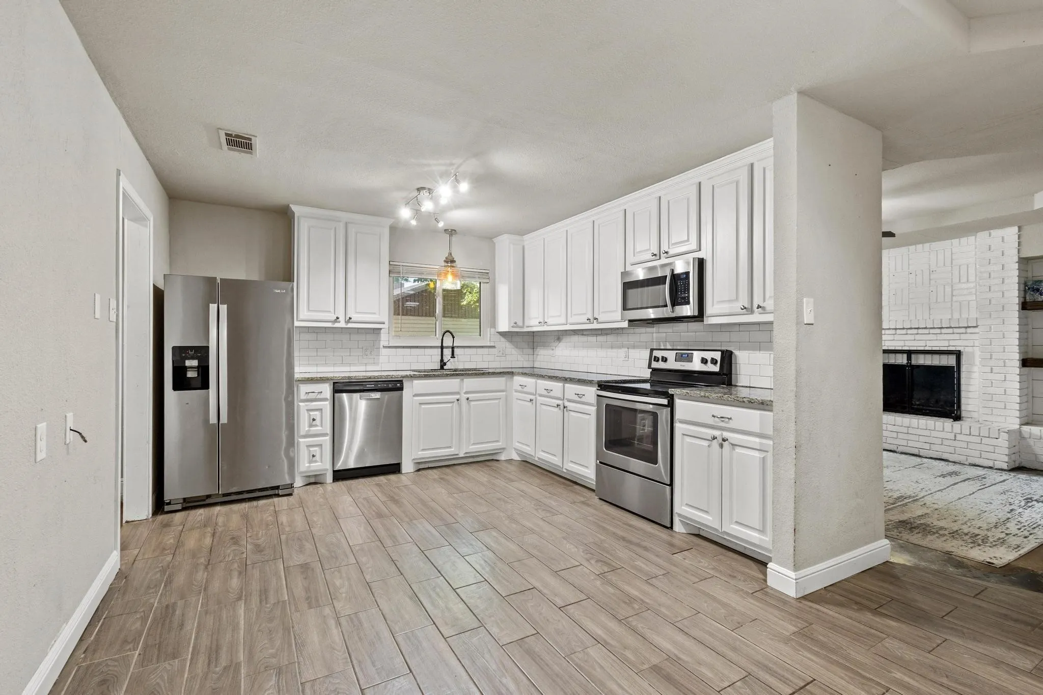 Kitchen featuring wood-finish flooring, white cabinetry, stainless steel appliances, and light-toned countertops