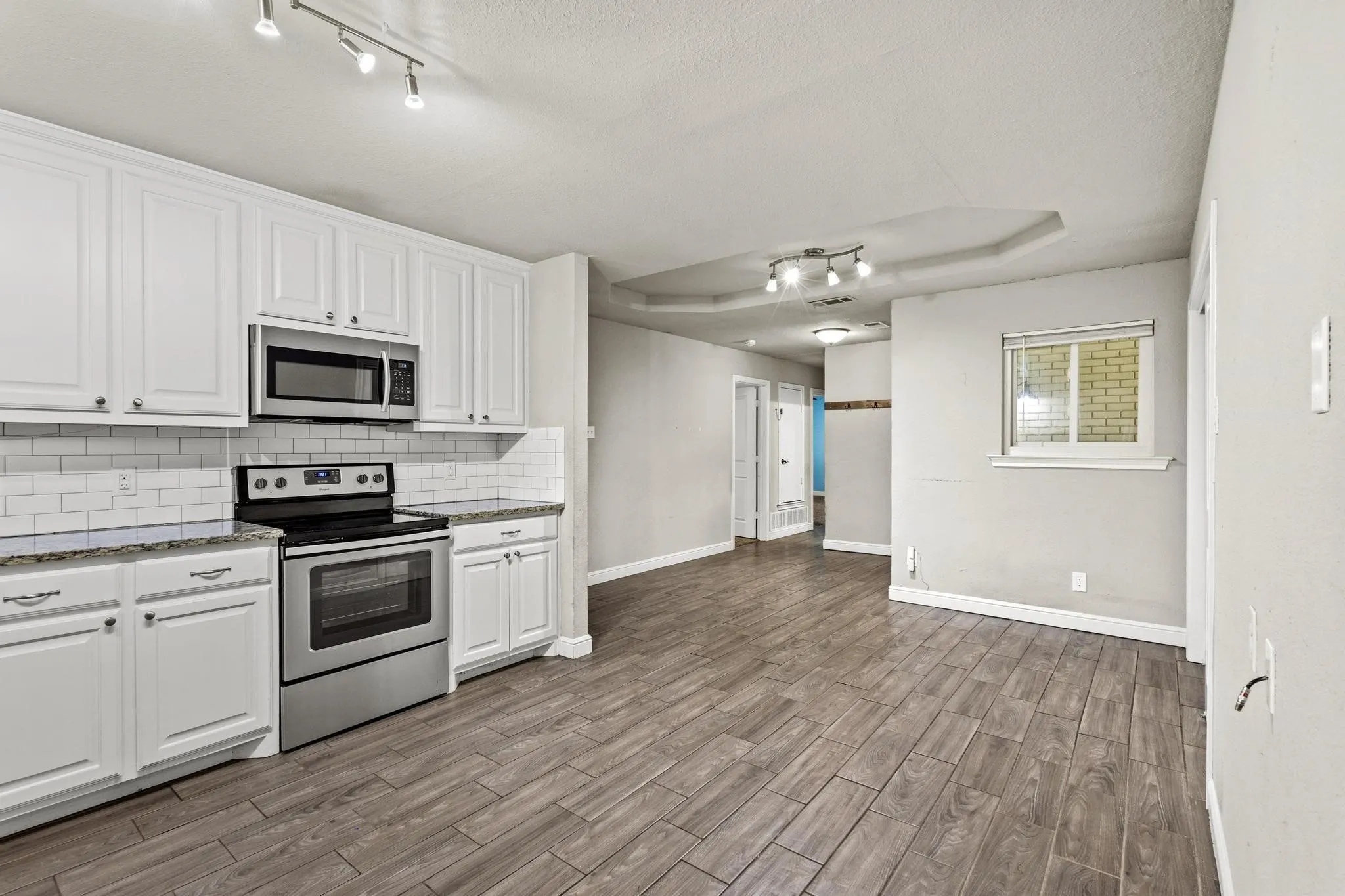 Kitchen featuring white cabinetry, subway tile backsplash, stainless steel appliances, wood-finish flooring, and recessed ceiling details