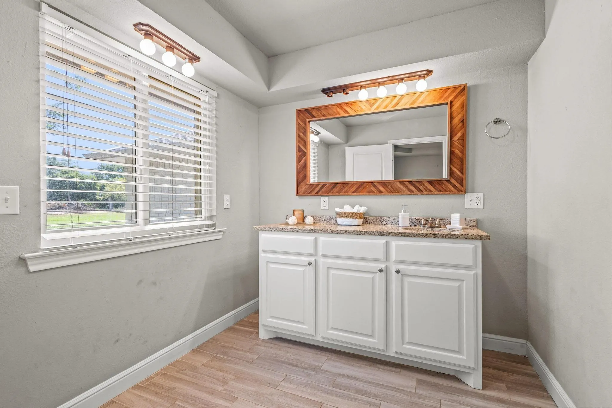 Bathroom featuring a single vanity with white cabinetry, a light-colored countertop, and a wood-finish framed mirror