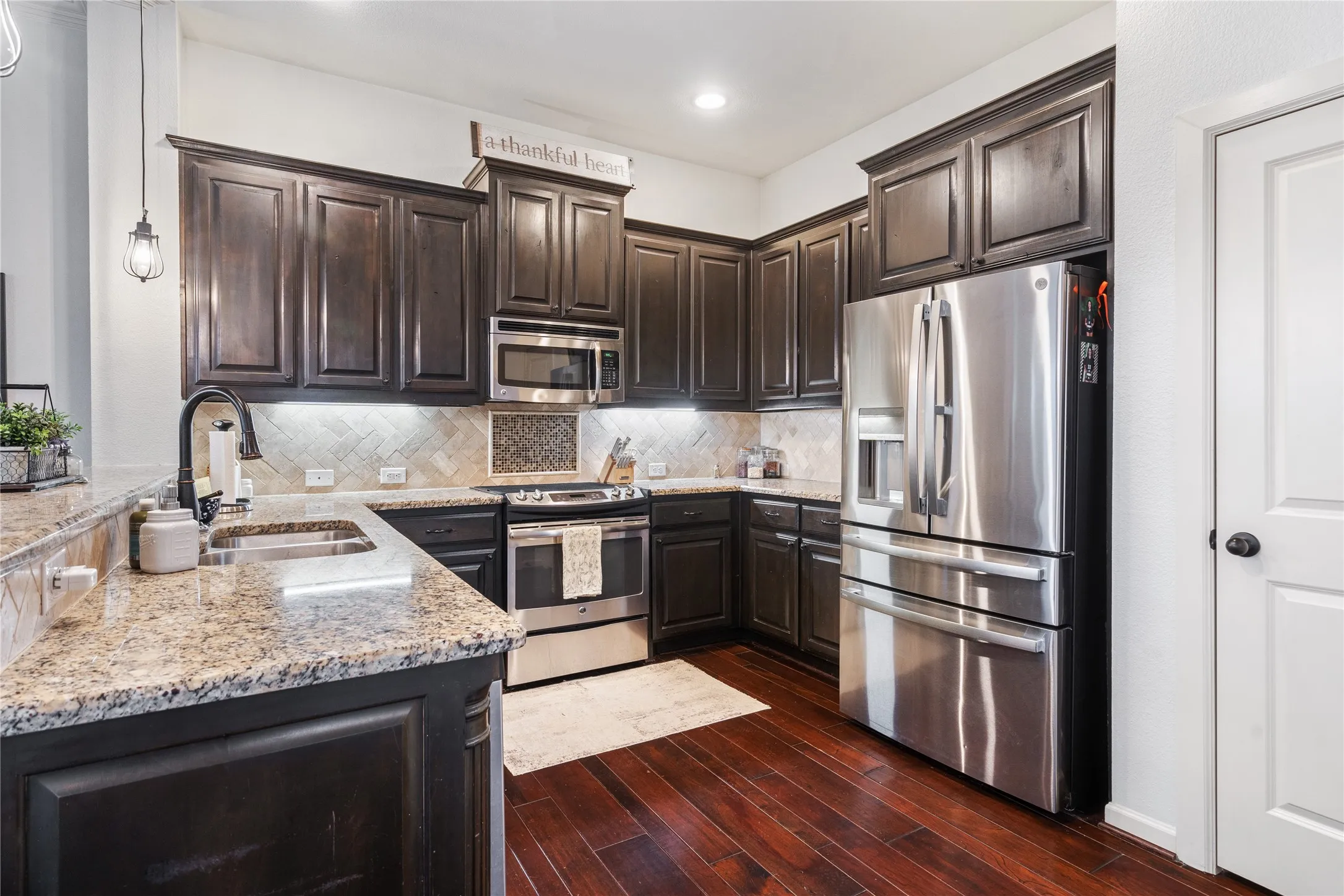 Kitchen featuring dark wood cabinetry, light granite countertops, stainless steel appliances, a herringbone tile backsplash, and pantry