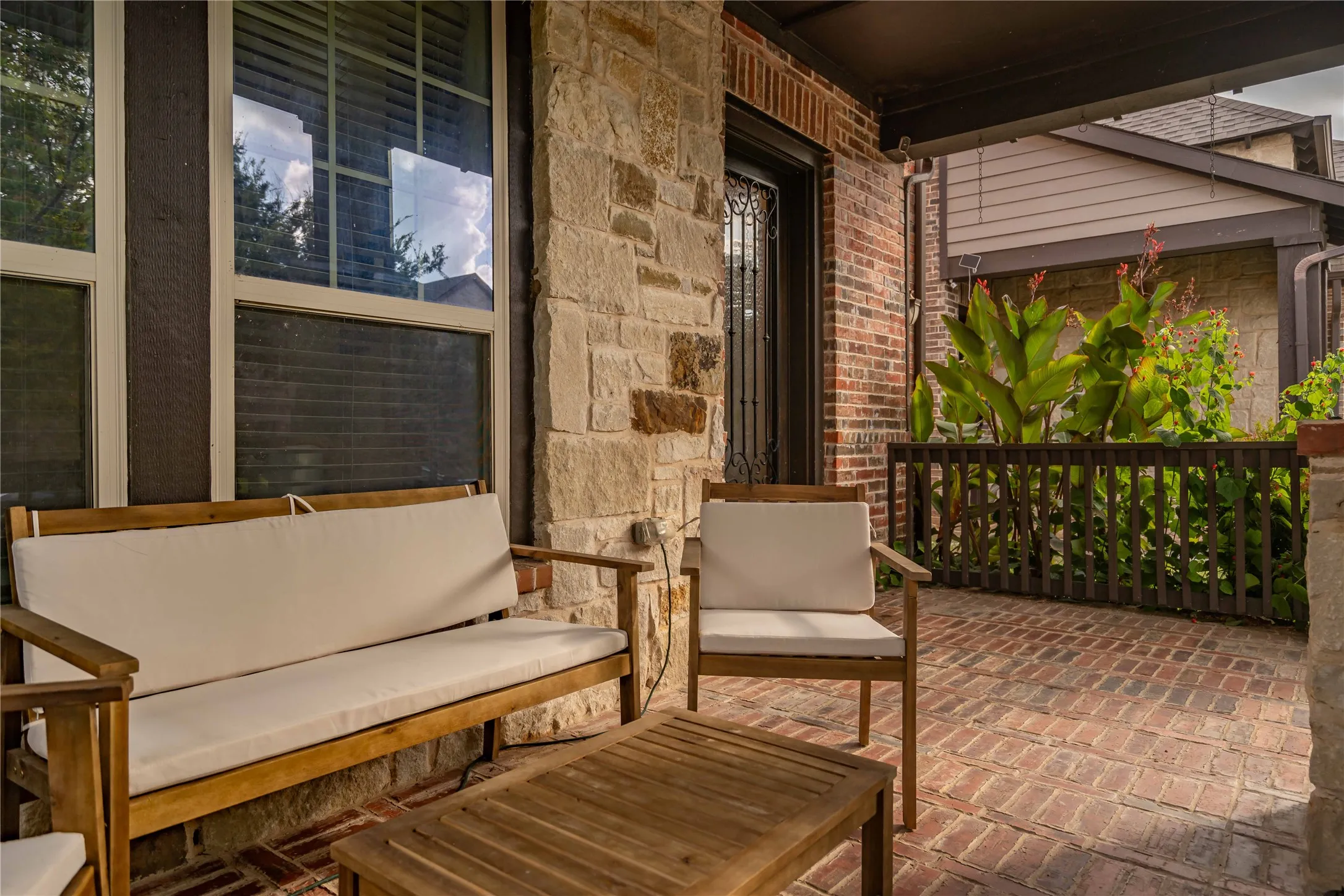 Covered front porch with brick pavers flooring, stone and brick exterior, and wood railing