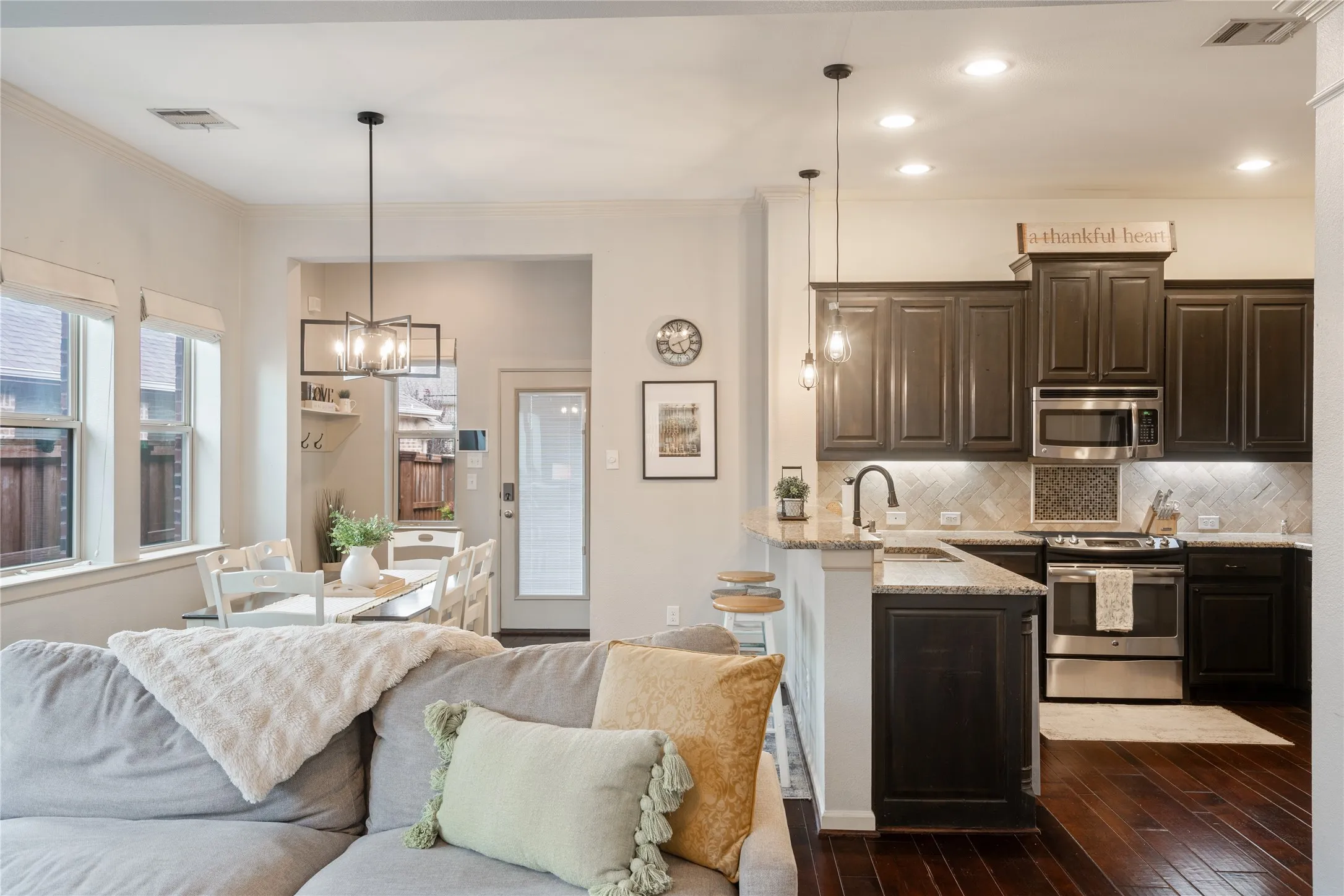 Open-concept kitchen and dining area featuring dark wood-finish cabinetry, stainless steel appliances, granite countertops with seating at the bar.