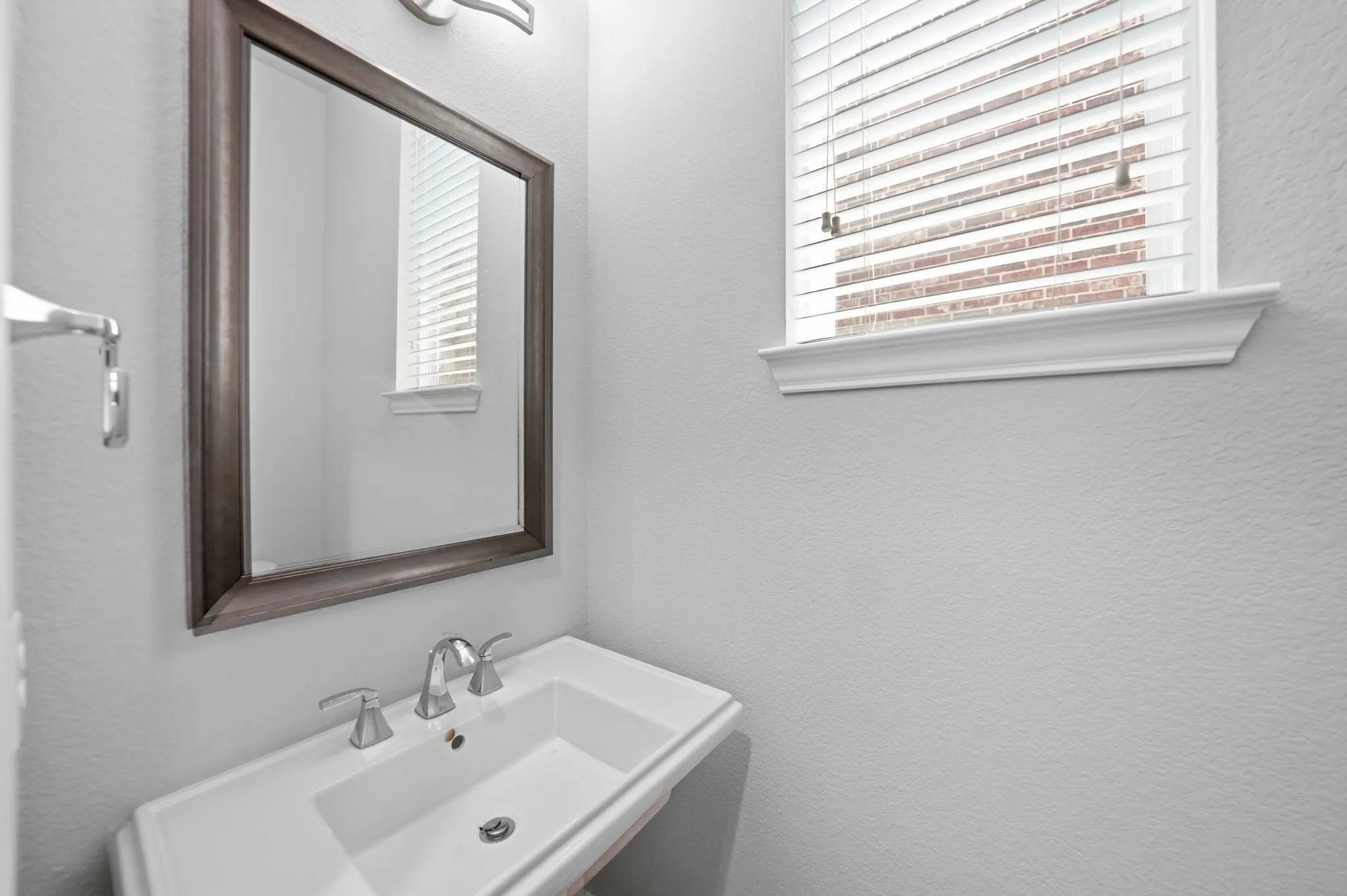 Powder room featuring a pedestal sink with chrome faucet, framed mirror, and a window with blinds