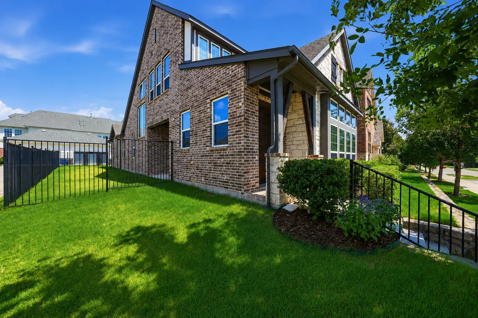 Brick and stone exterior featuring a covered entry, gabled roofline, multiple windows, and a fenced yard with established landscaping