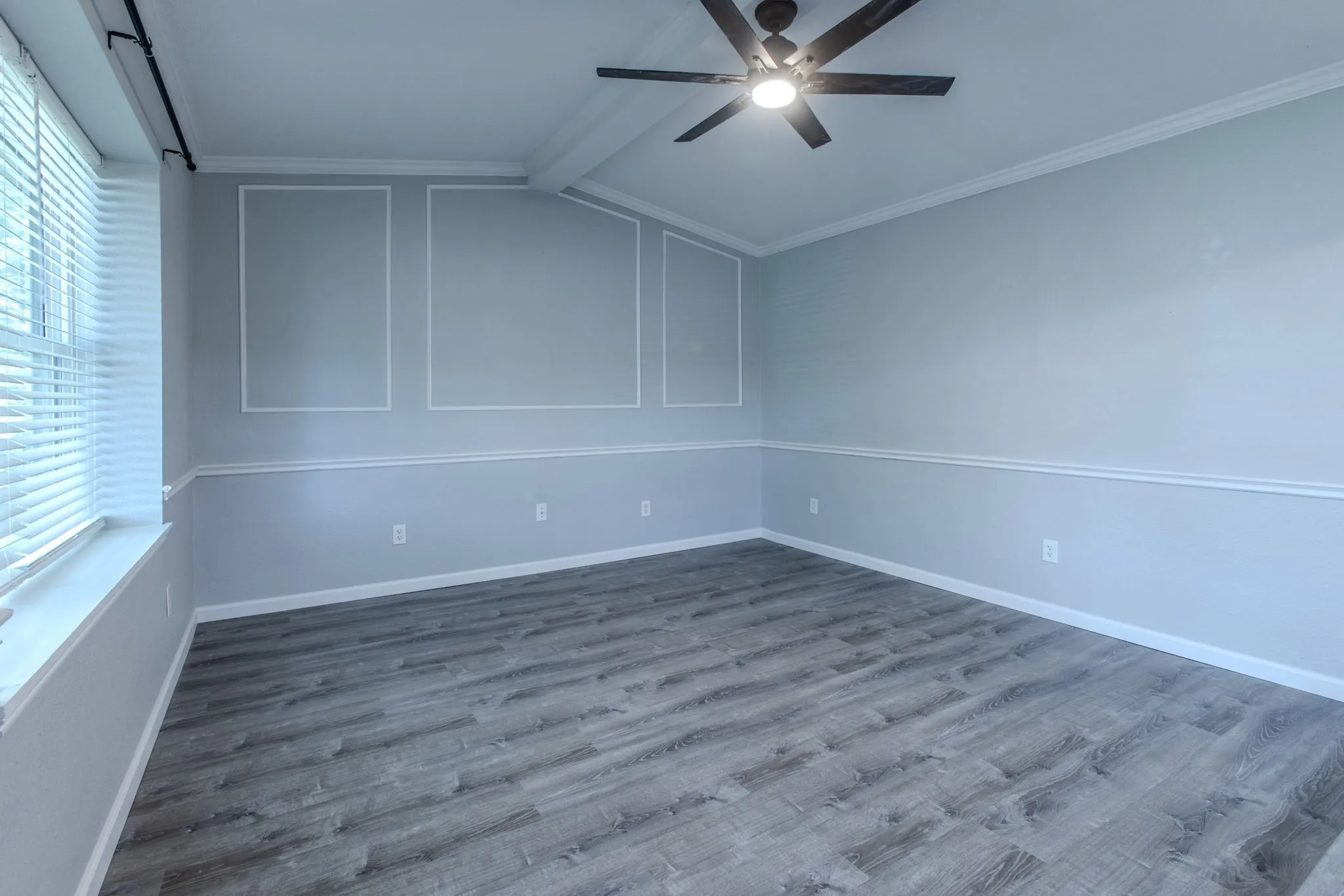 Spacious room featuring wood-finish flooring, a ceiling fan with integrated lighting, window blinds, decorative wall molding, and crown molding