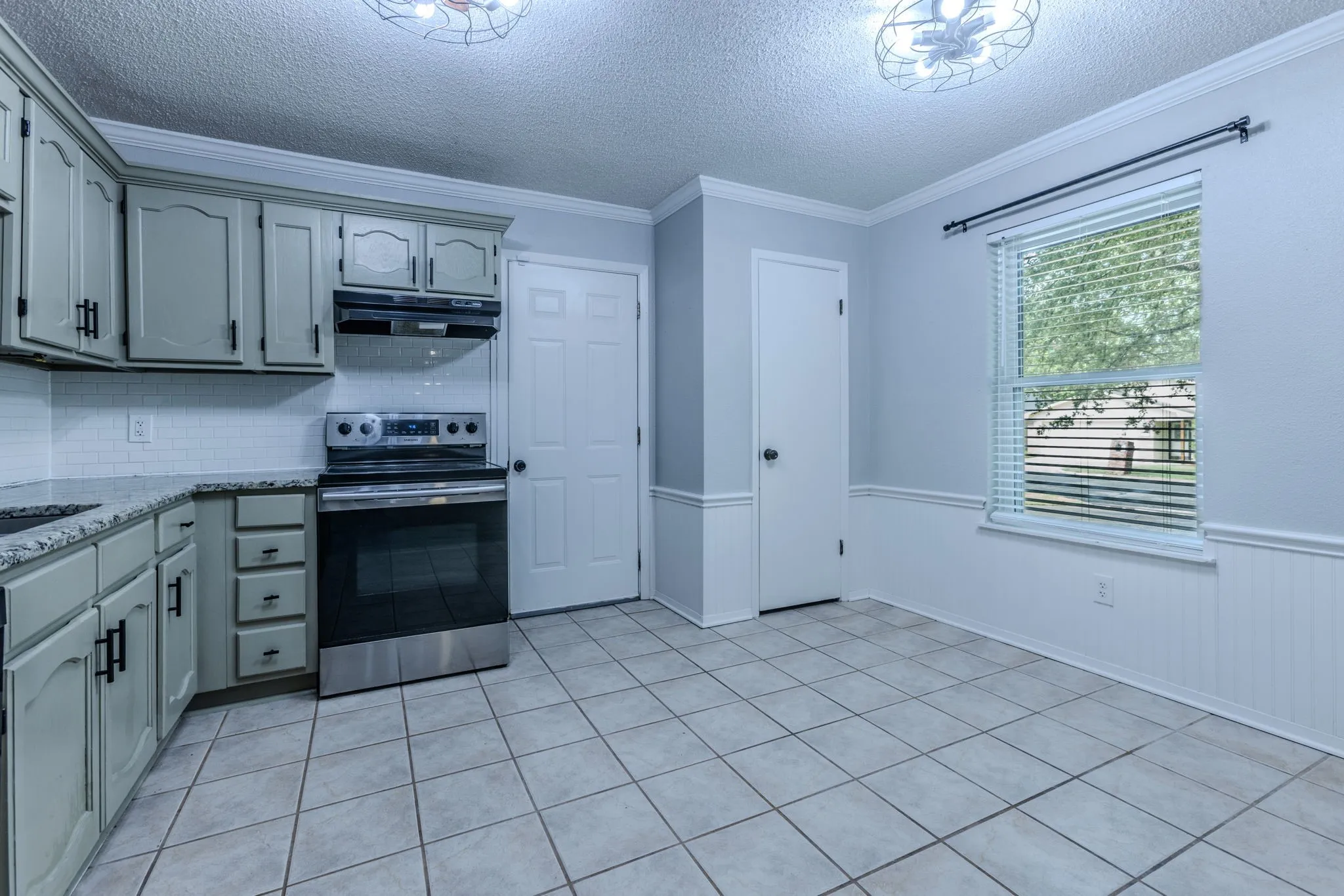 Kitchen featuring light-toned cabinetry, granite-style countertops, a tile backsplash, and stainless steel appliances