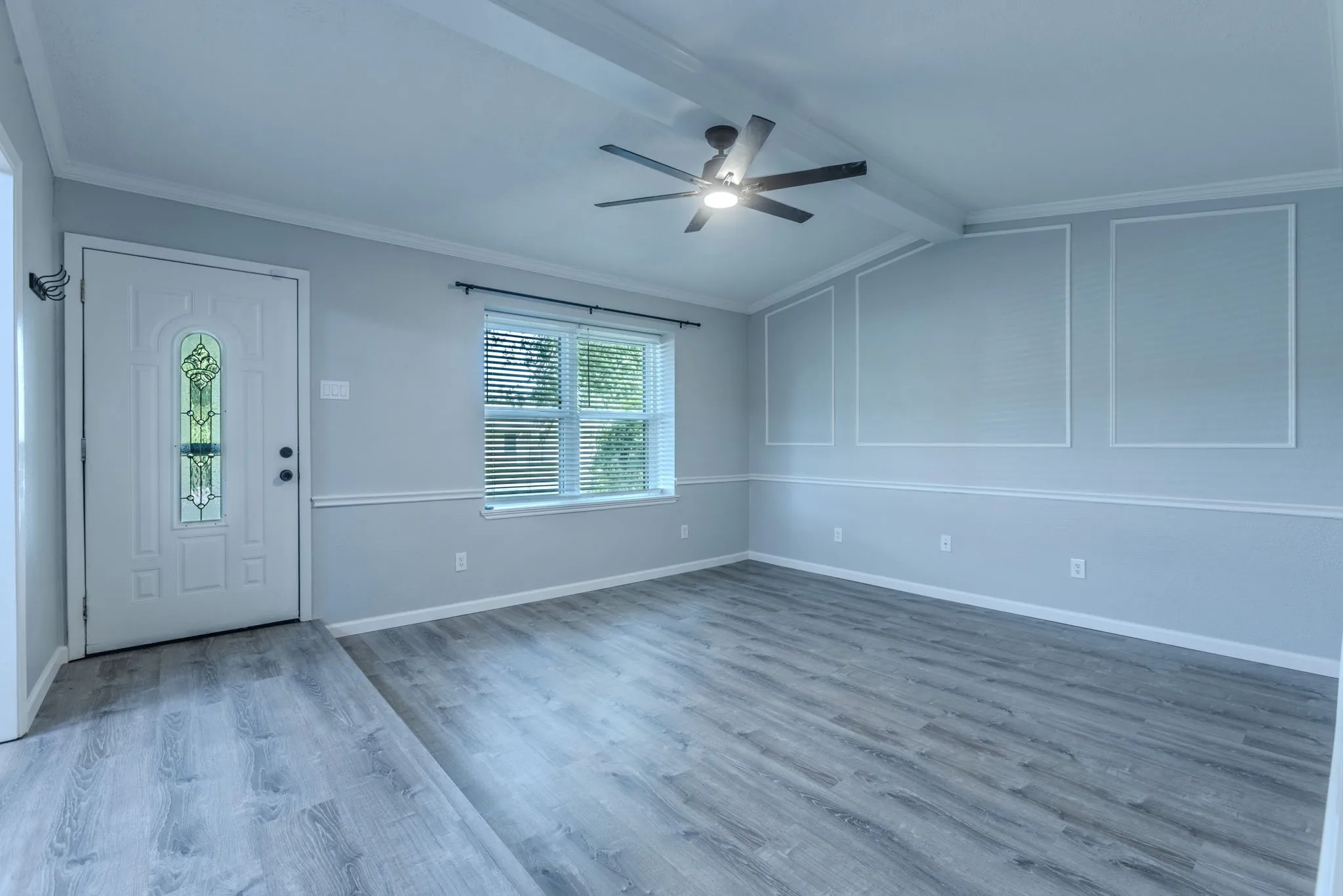 Spacious interior featuring wood-finish flooring, a decorative entry door with leaded glass, and a modern ceiling fan