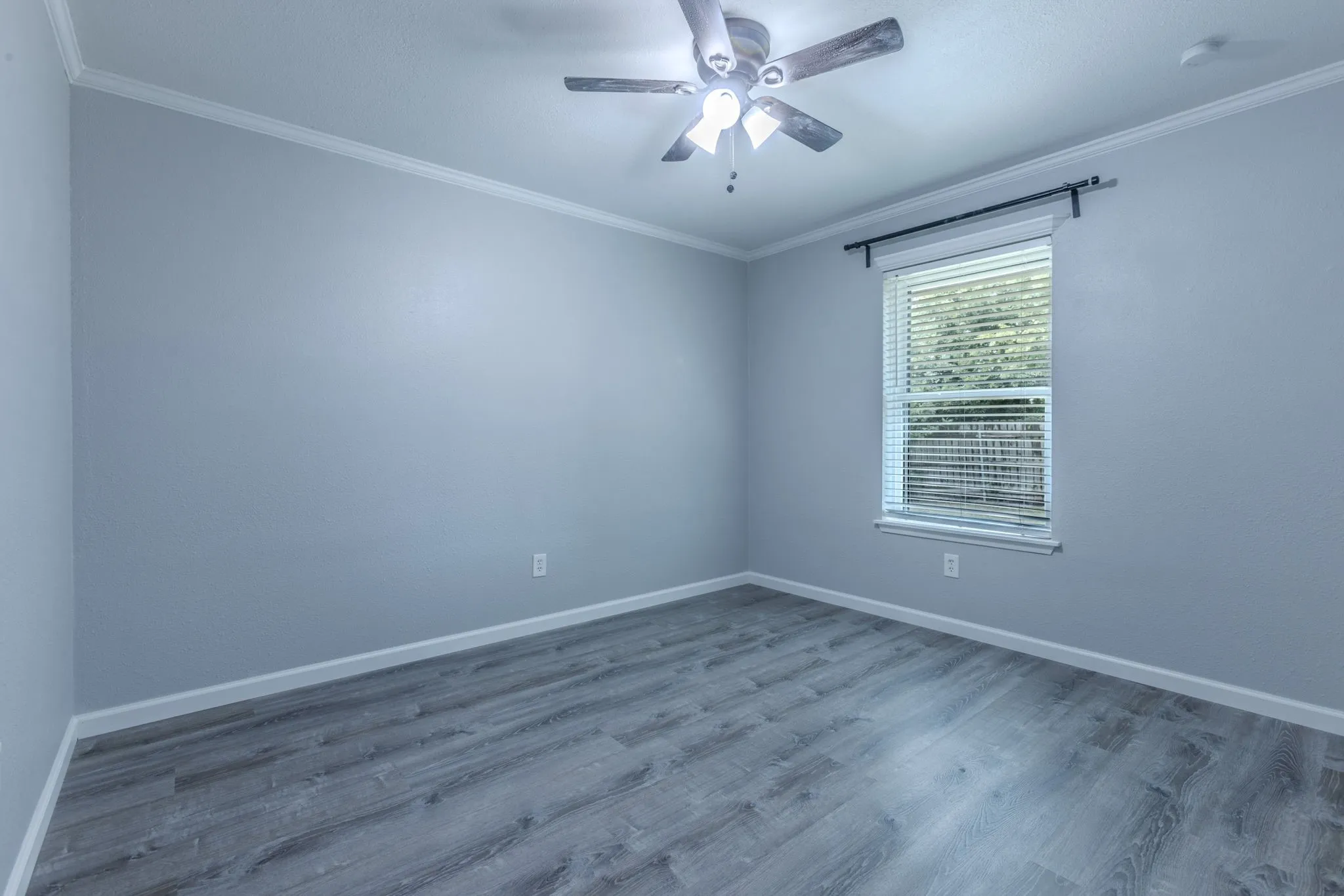 Room featuring wood-finish flooring, a ceiling fan with integrated lighting, and a single window with blinds and curtain rod