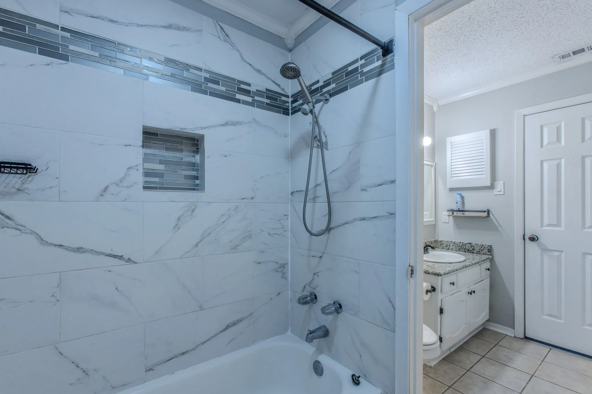 Bathtub shower combination featuring white marble-look tile, a decorative glass tile accent band, and a tiled shower niche