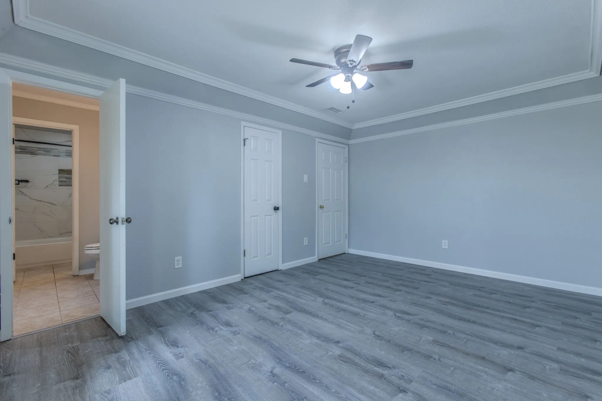 Spacious interior room featuring wood-finish flooring, light gray wall paint, and white crown molding