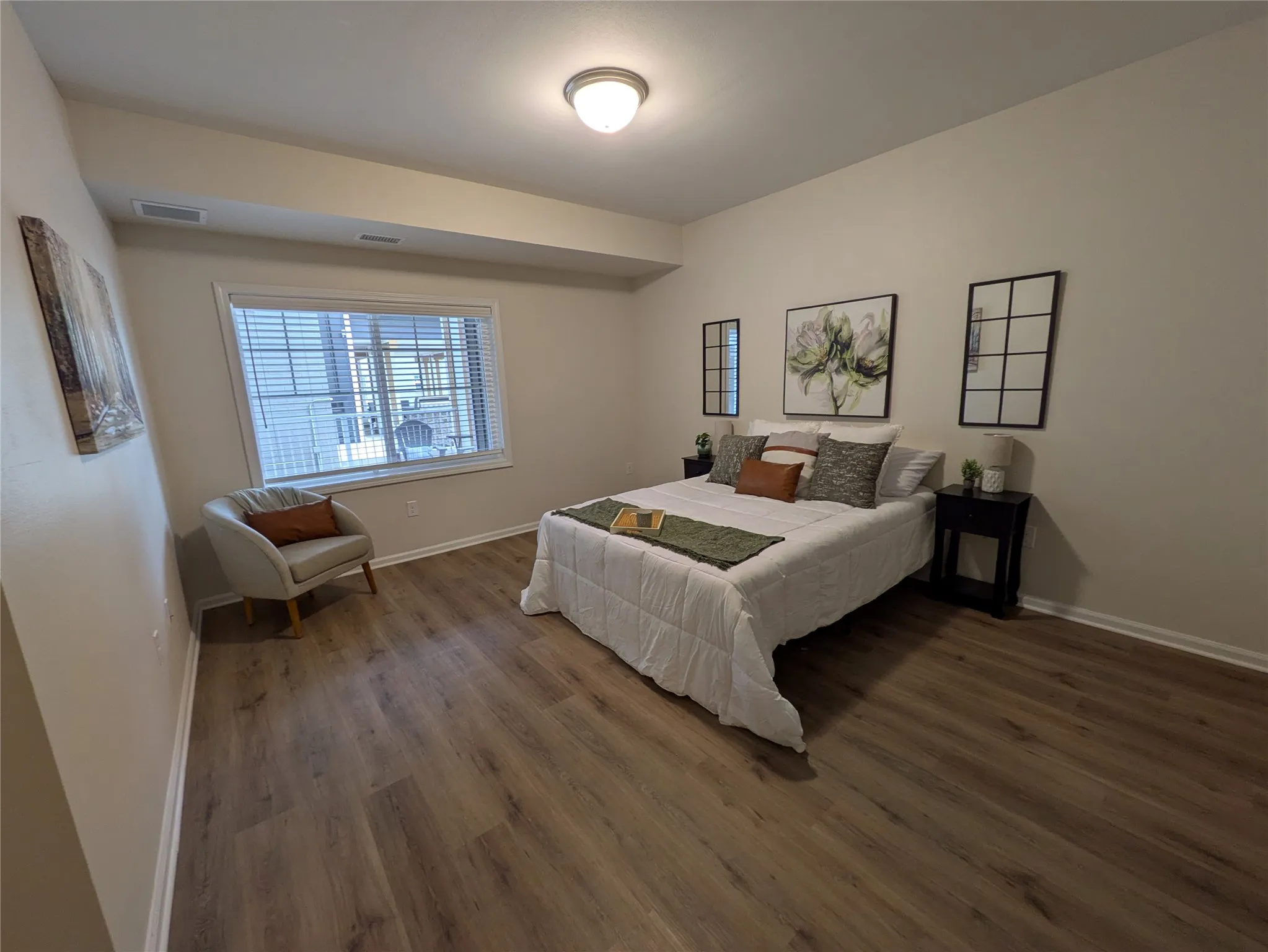 Spacious bedroom featuring wood-finish flooring, ample natural light from a window with blinds, and recessed lighting