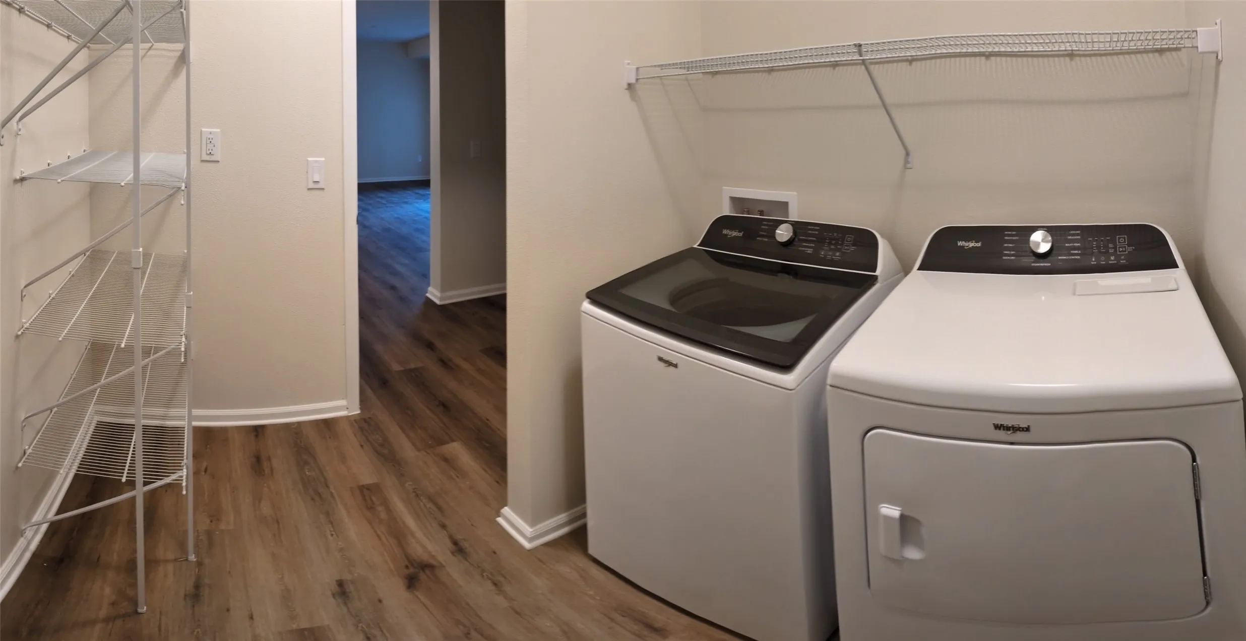 Dedicated laundry area featuring modern white washer and dryer units, overhead wire shelving, and wood-finish flooring