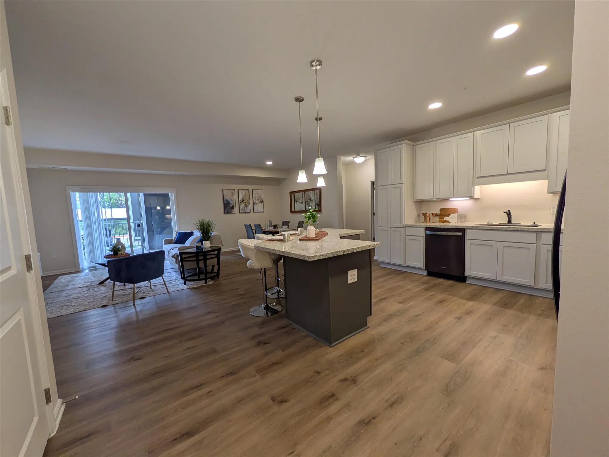 Open-concept living space featuring wood-finish flooring, a kitchen island with pendant lighting, light-toned cabinetry, and recessed ceiling lighting