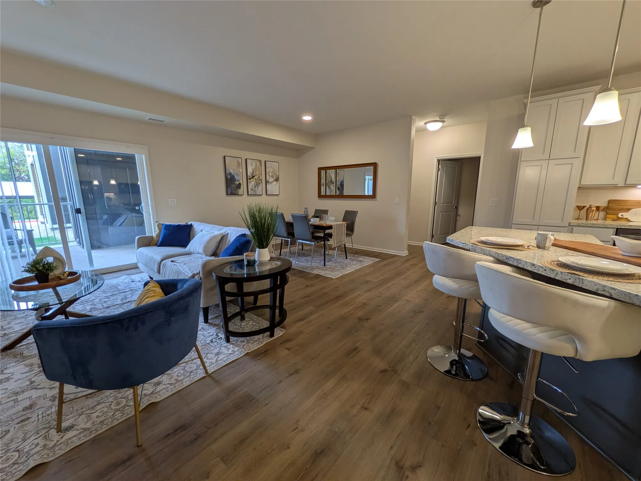 Open-concept living space featuring wood-finish flooring, a kitchen island with pendant lighting, white shaker cabinetry, and a dining area