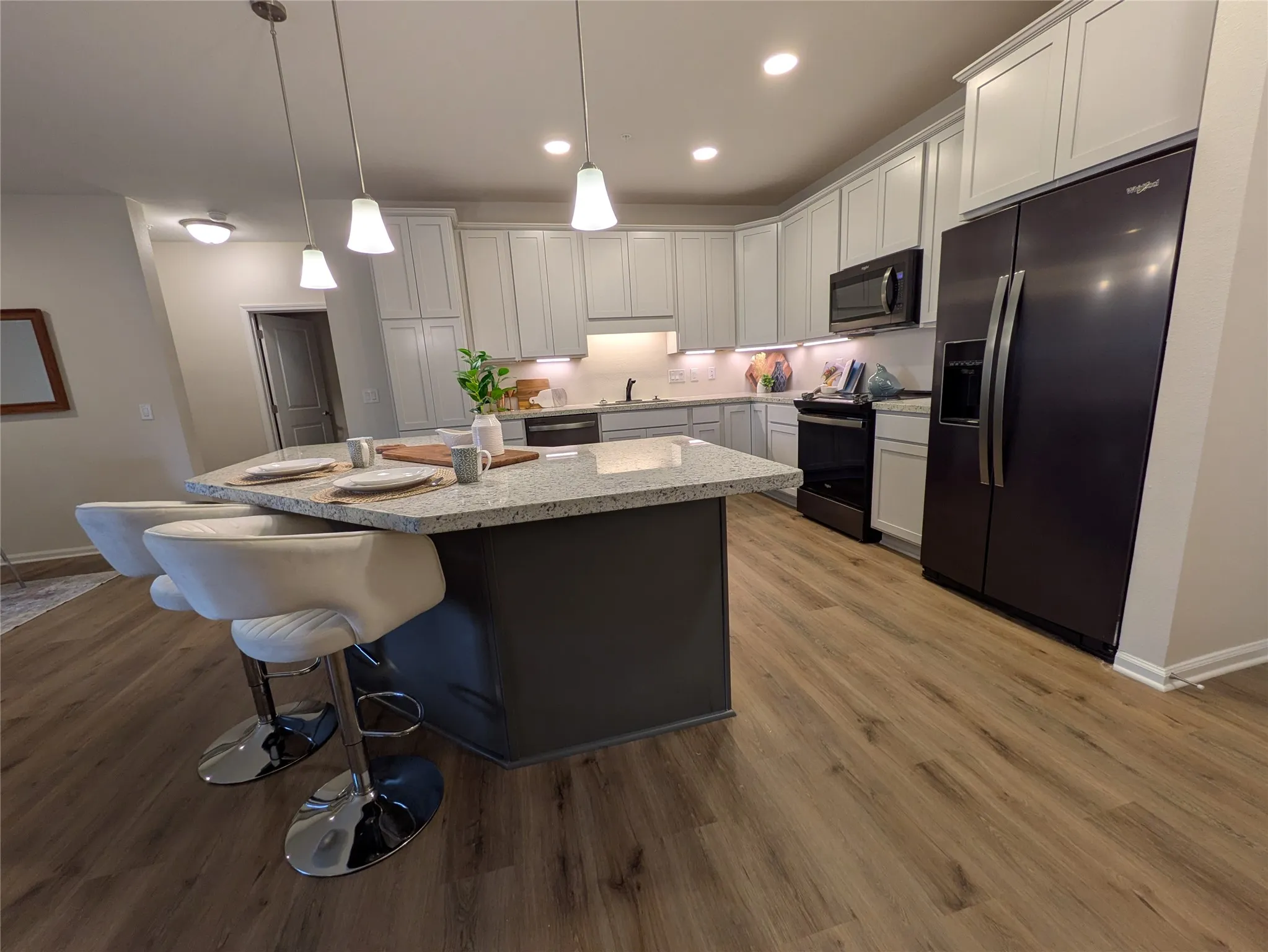 Modern kitchen featuring an expansive center island with stone-finish countertop, light-toned cabinetry, wood-finish flooring, and pendant lighting