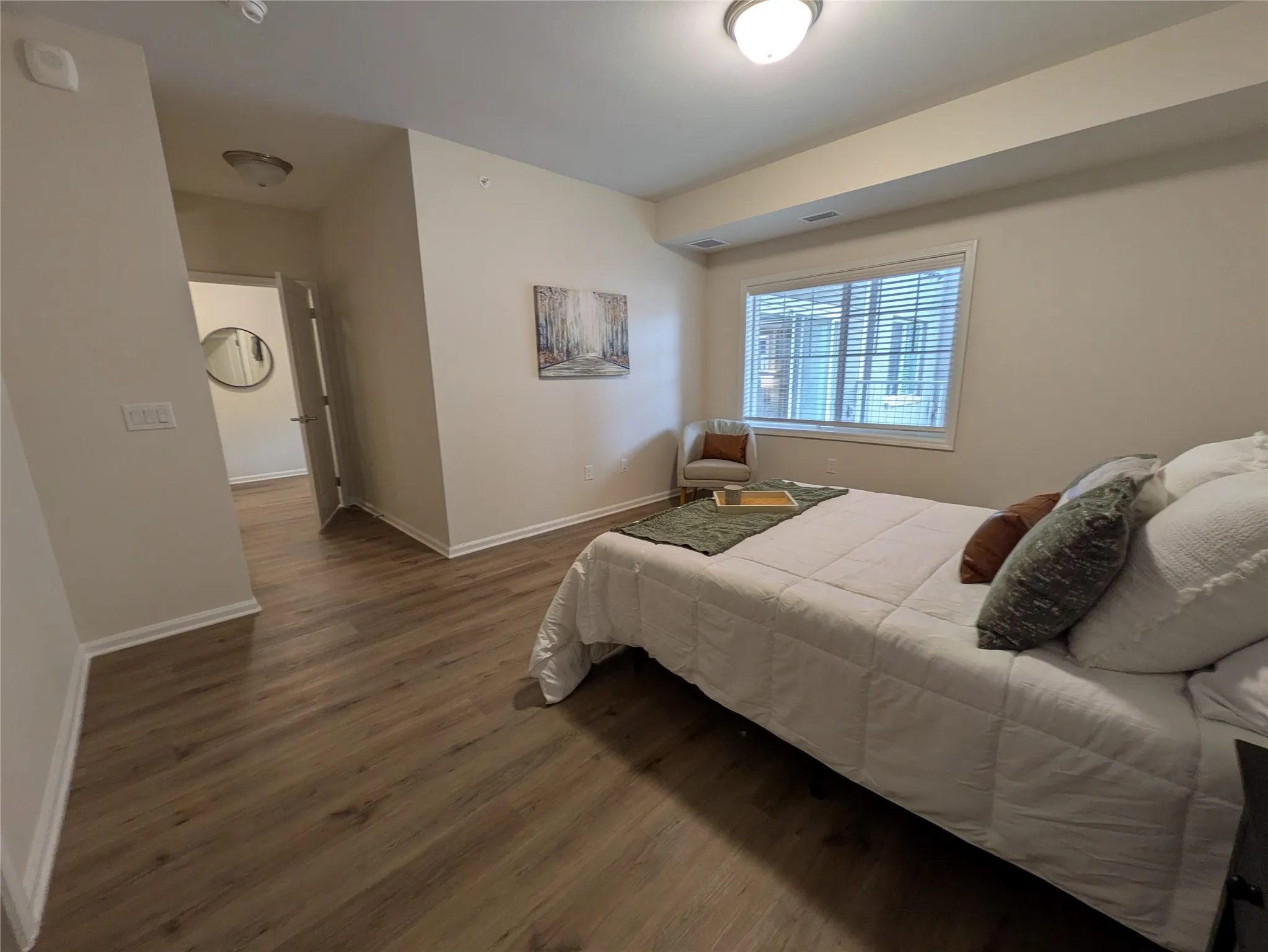 Bedroom featuring wood-finish flooring, a large window with blinds, and neutral wall tones