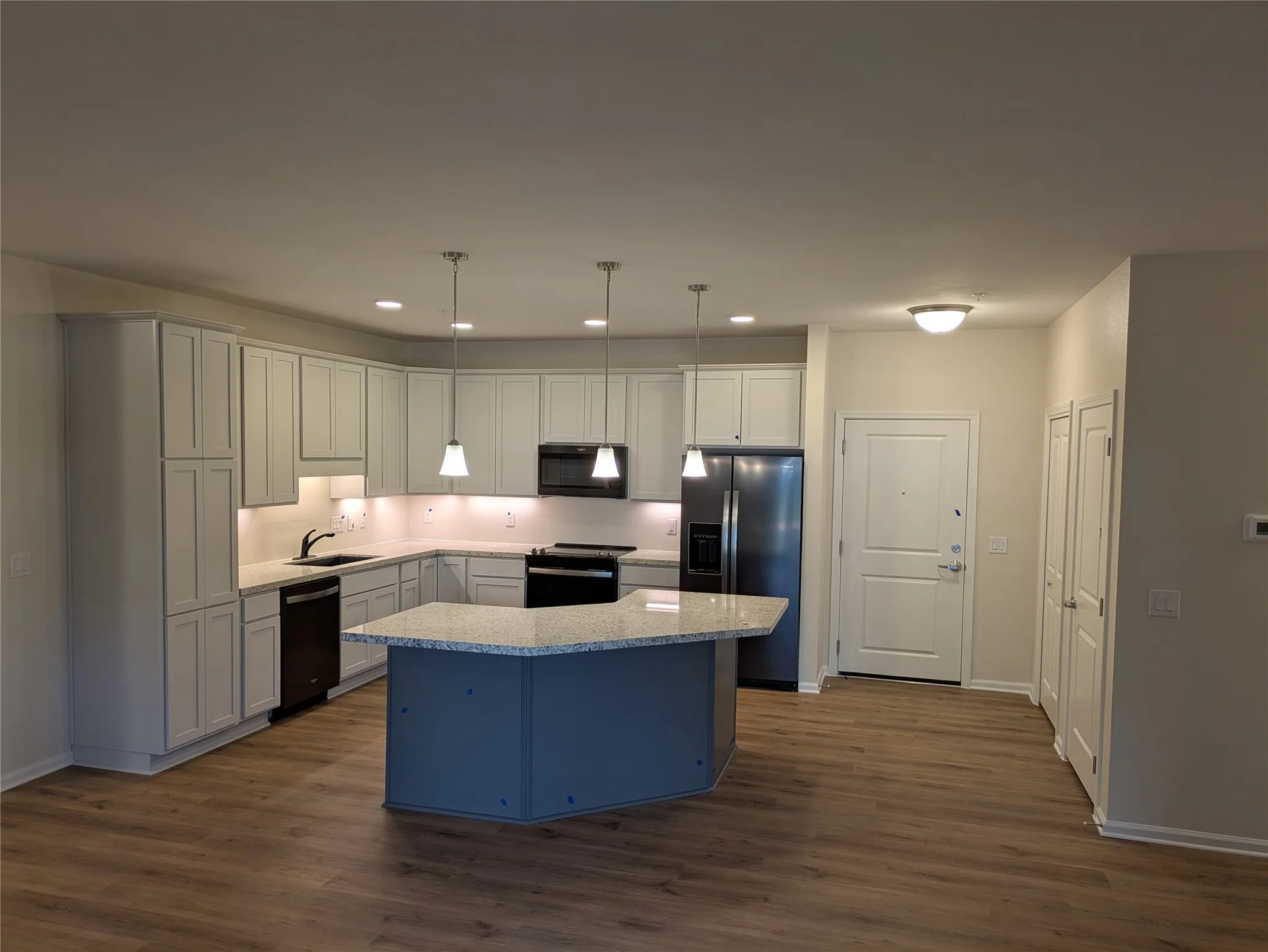 Open-concept kitchen featuring extensive light gray cabinetry, a central island with a contrasting base, granite countertops, and wood-finish flooring