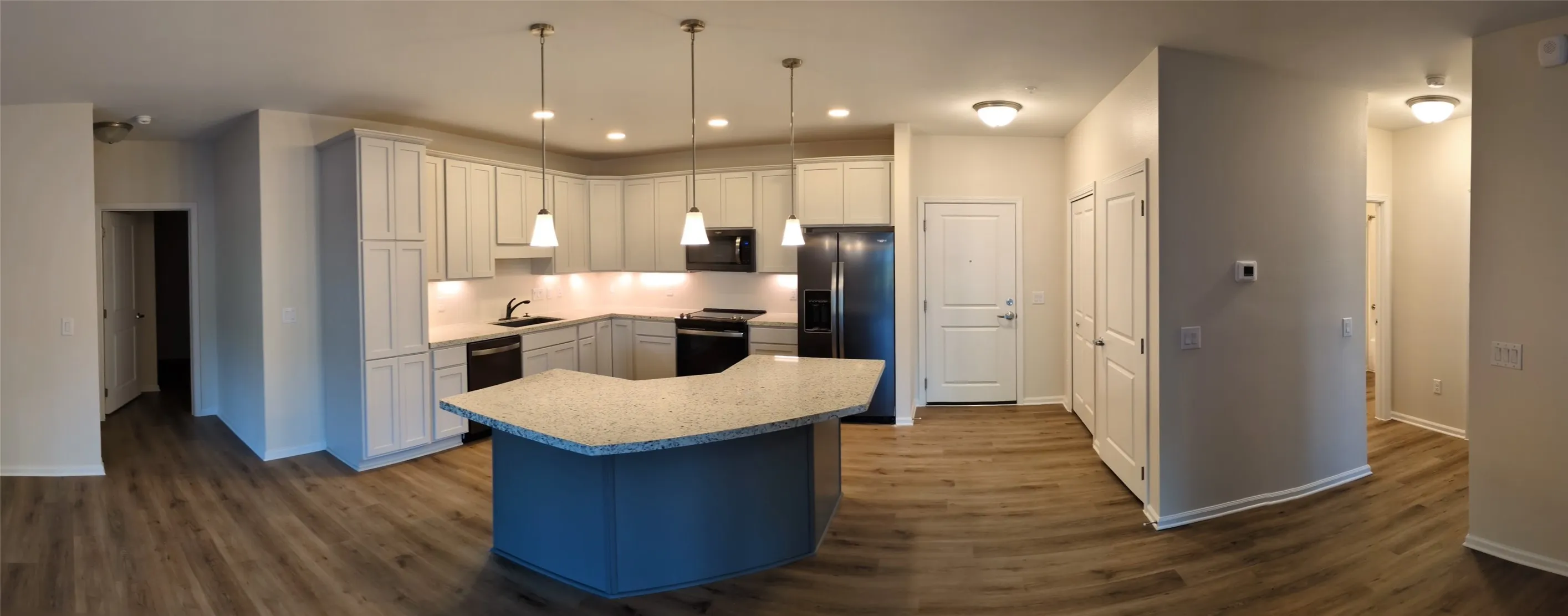 Kitchen featuring a U-shaped island with a light-toned countertop, pendant lighting, built-in black appliances, white cabinetry, and wood-finish flooring