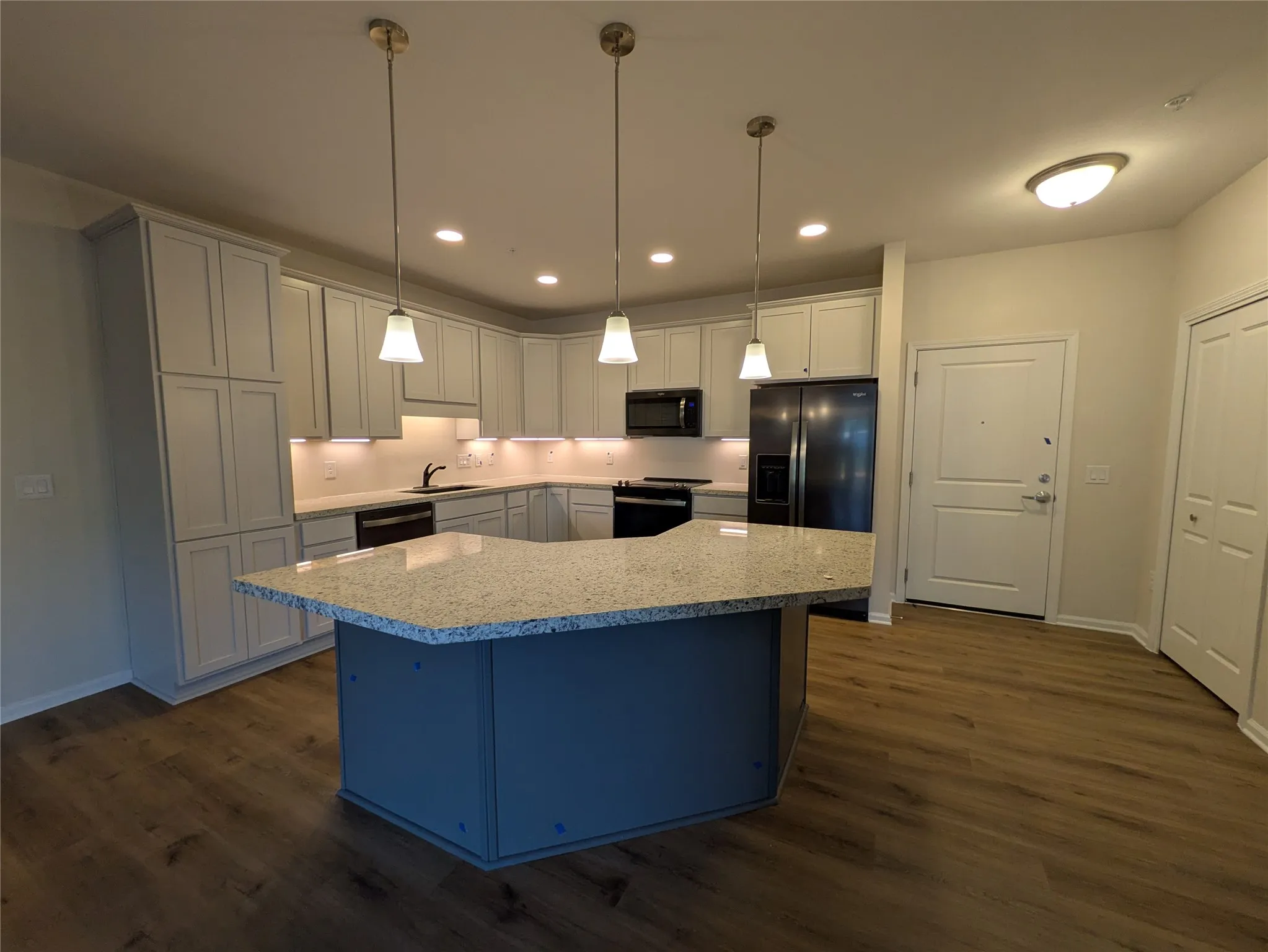 Spacious kitchen featuring an expansive island with a granite-style countertop, white shaker cabinetry, stainless steel appliances, and wood-finish flooring