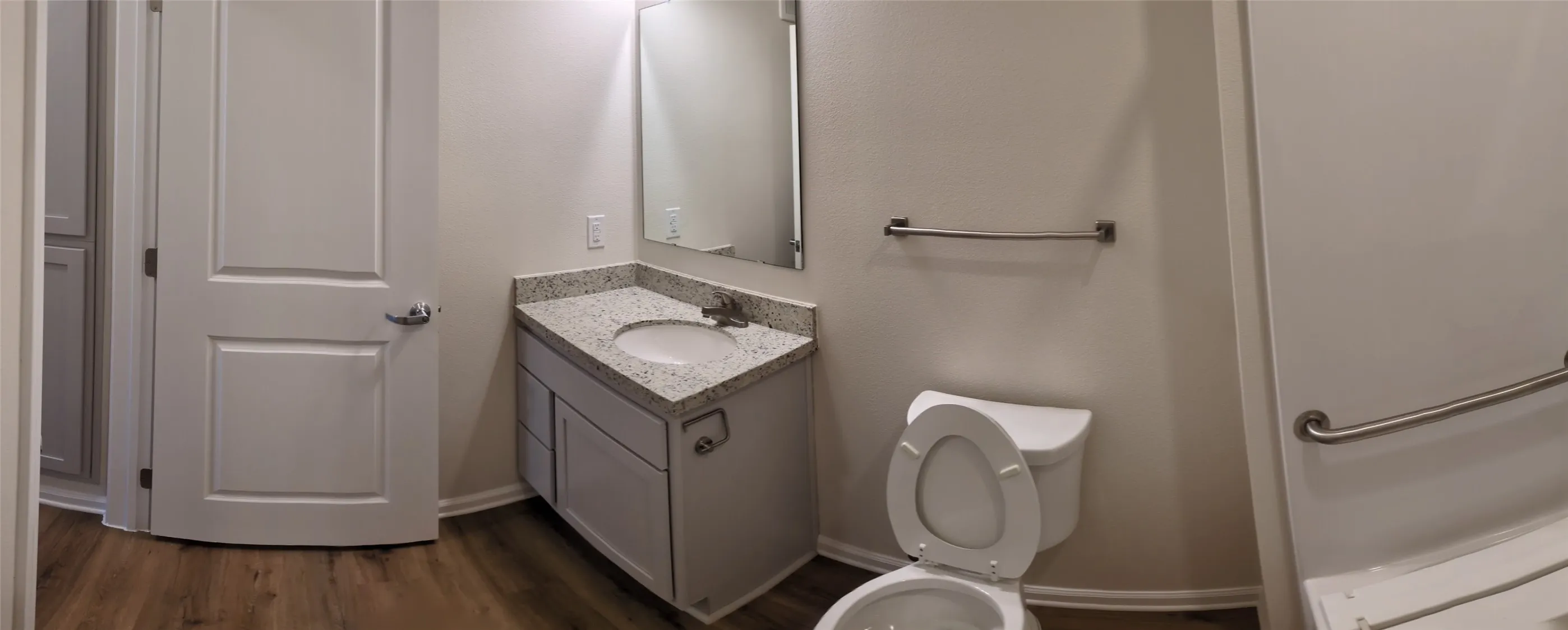 Bathroom featuring a white vanity with a speckled countertop, undermount sink, and wood-finish flooring