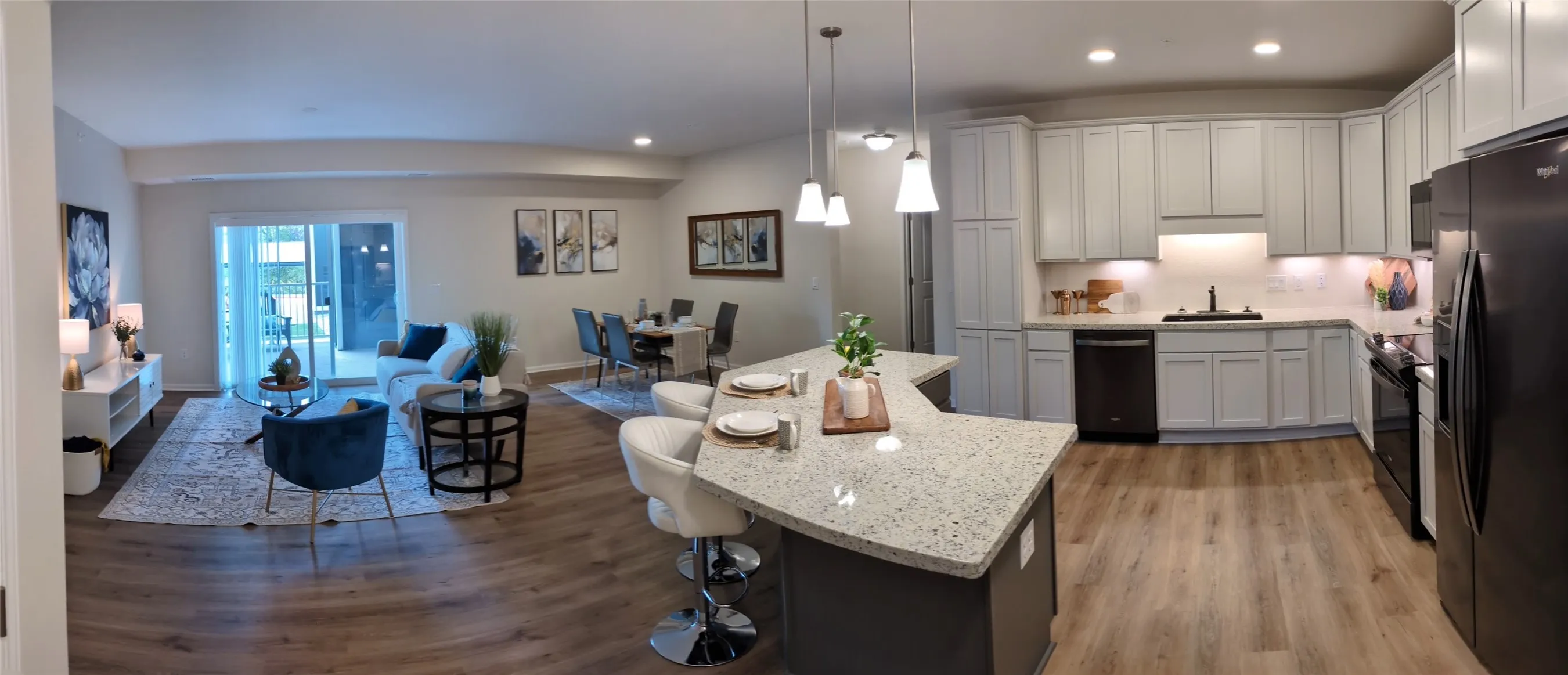 Open-concept living space featuring wood-finish flooring, a kitchen island with seating, pendant lighting, white cabinetry, and stainless steel appliances