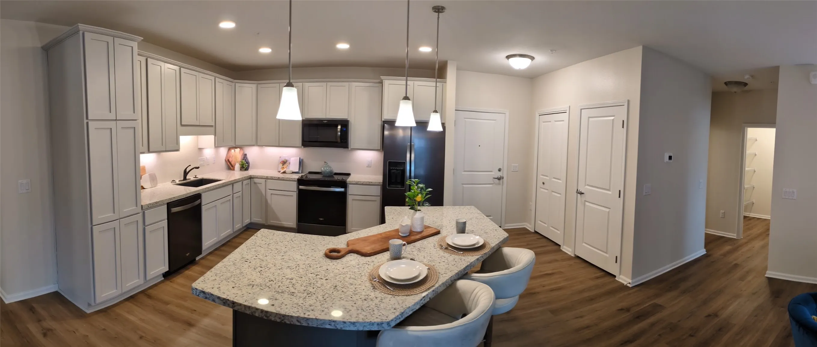 Kitchen featuring an island with stone-finish countertop, pendant lighting, wood-finish flooring, white cabinetry, and black appliances