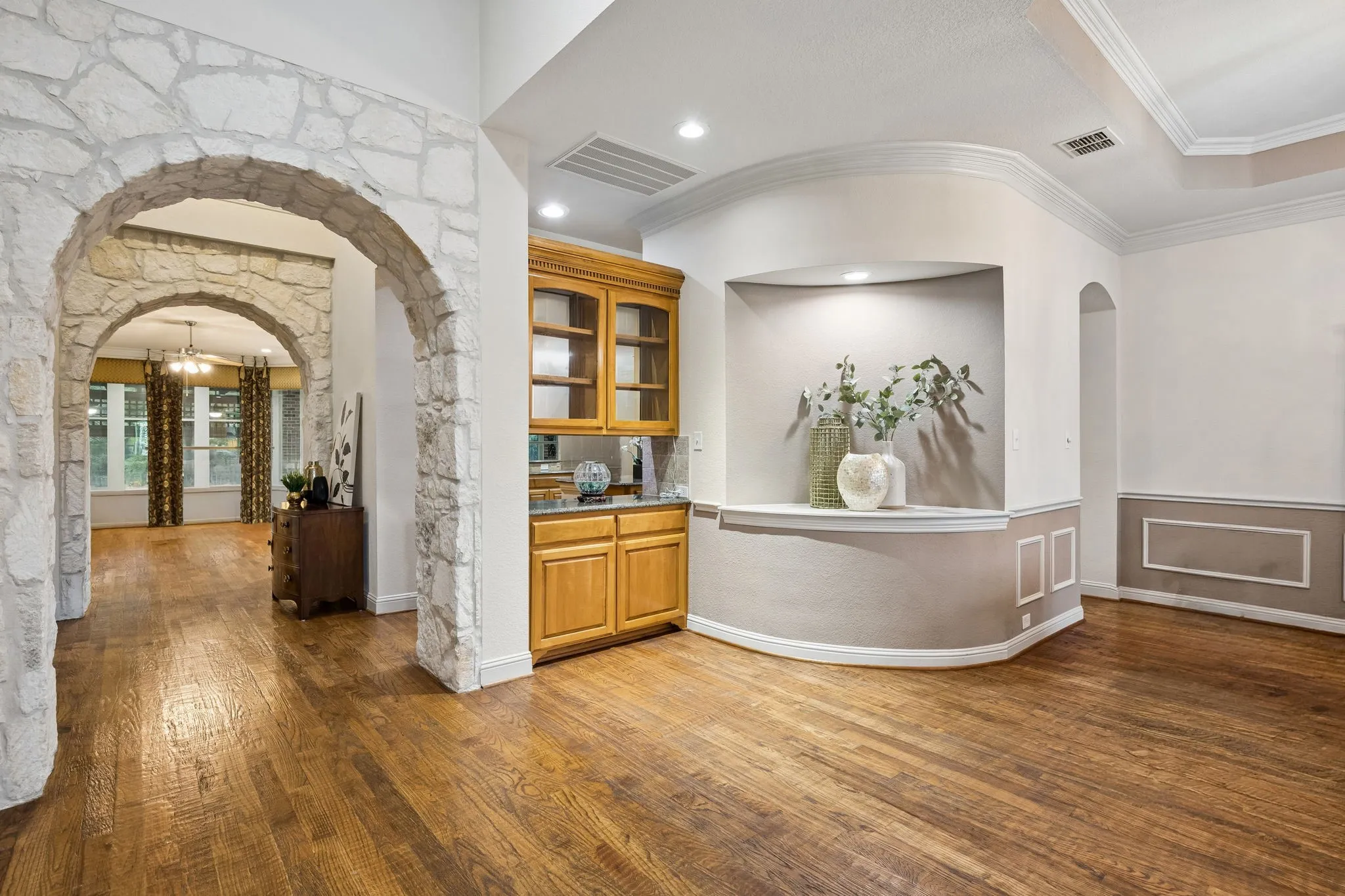 The entry opens to the spacious dining room.
Lovely art niche adds a hint of whimsy to the
space. Notice you have a pass through bar with
glass front cabinets for ease of entertaining. The
arched opening to the right leads to the kitchen.
Find handsome hand scraped hardwood flooring
through much of the first floor. Graceful arched
openings (including these encased in stonework)
are found throughout the home.