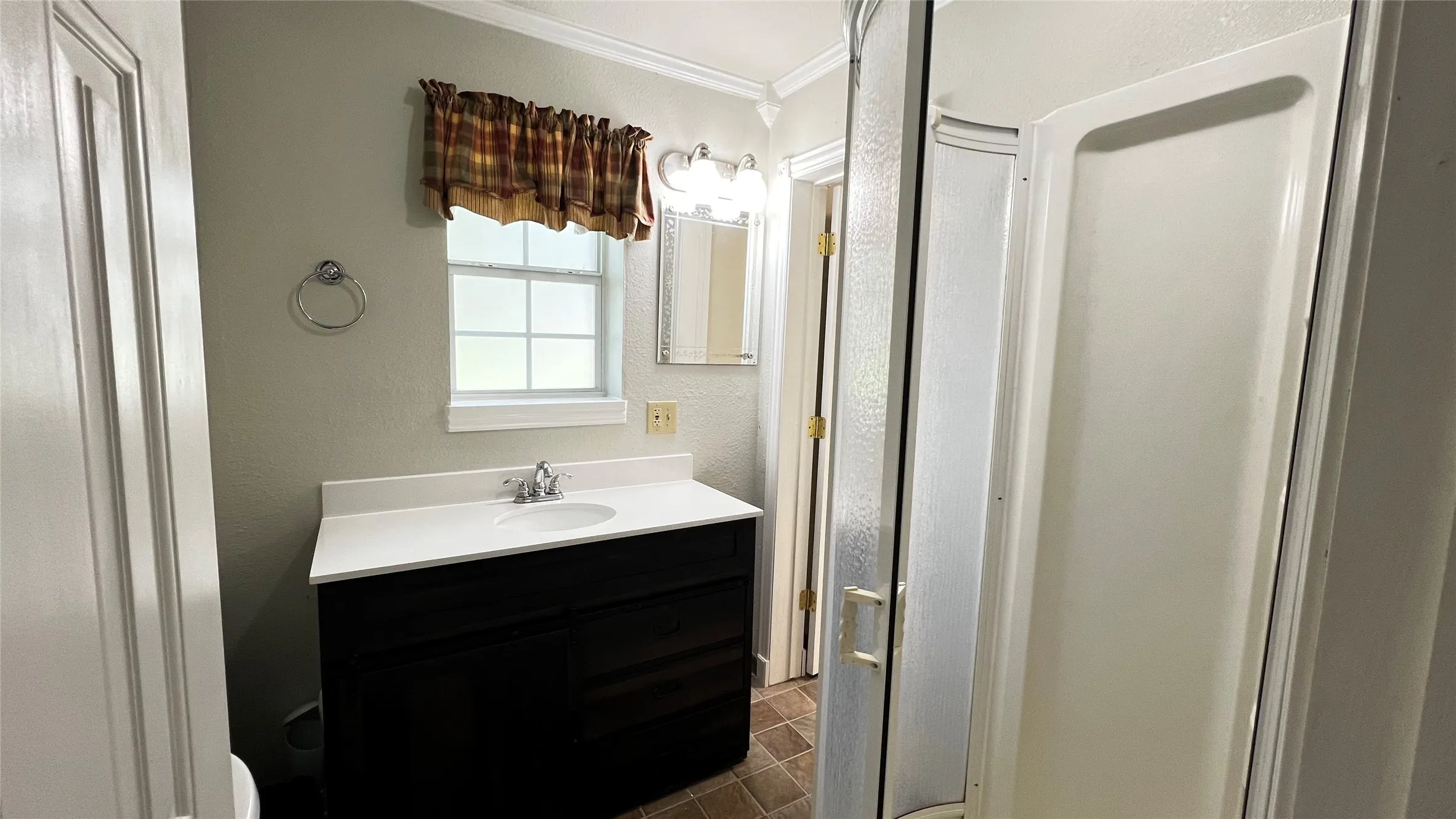 Ensuite downstairs Bathroom featuring a dark wood vanity with white countertop and integrated sink, a built-in shower stall, a window, and tiled flooring.  Access to Laundry room and Primary Bedroom.