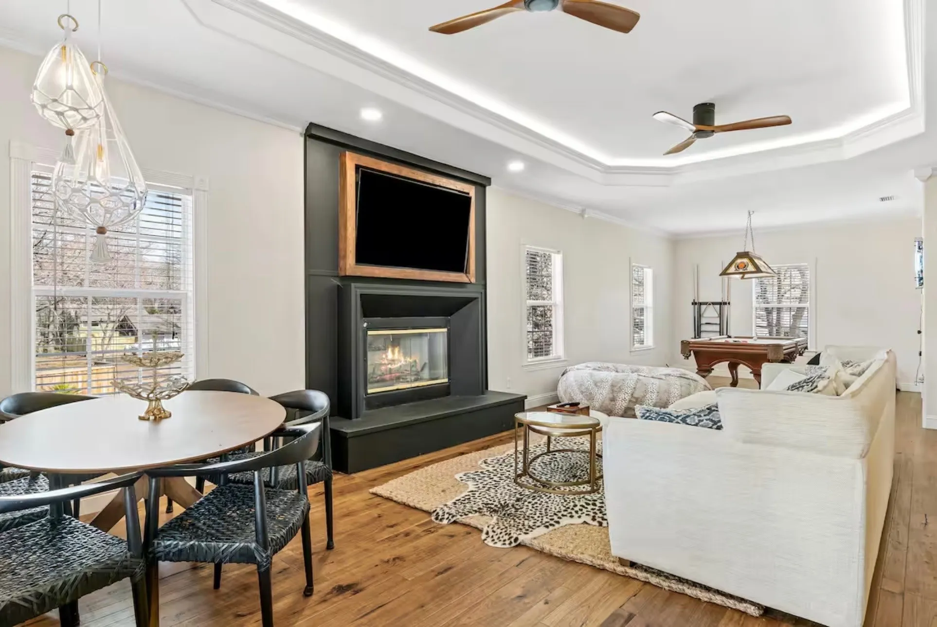 Open-concept living area featuring rich wood-finish flooring, a modern fireplace with a black surround, and a tray ceiling with recessed lighting