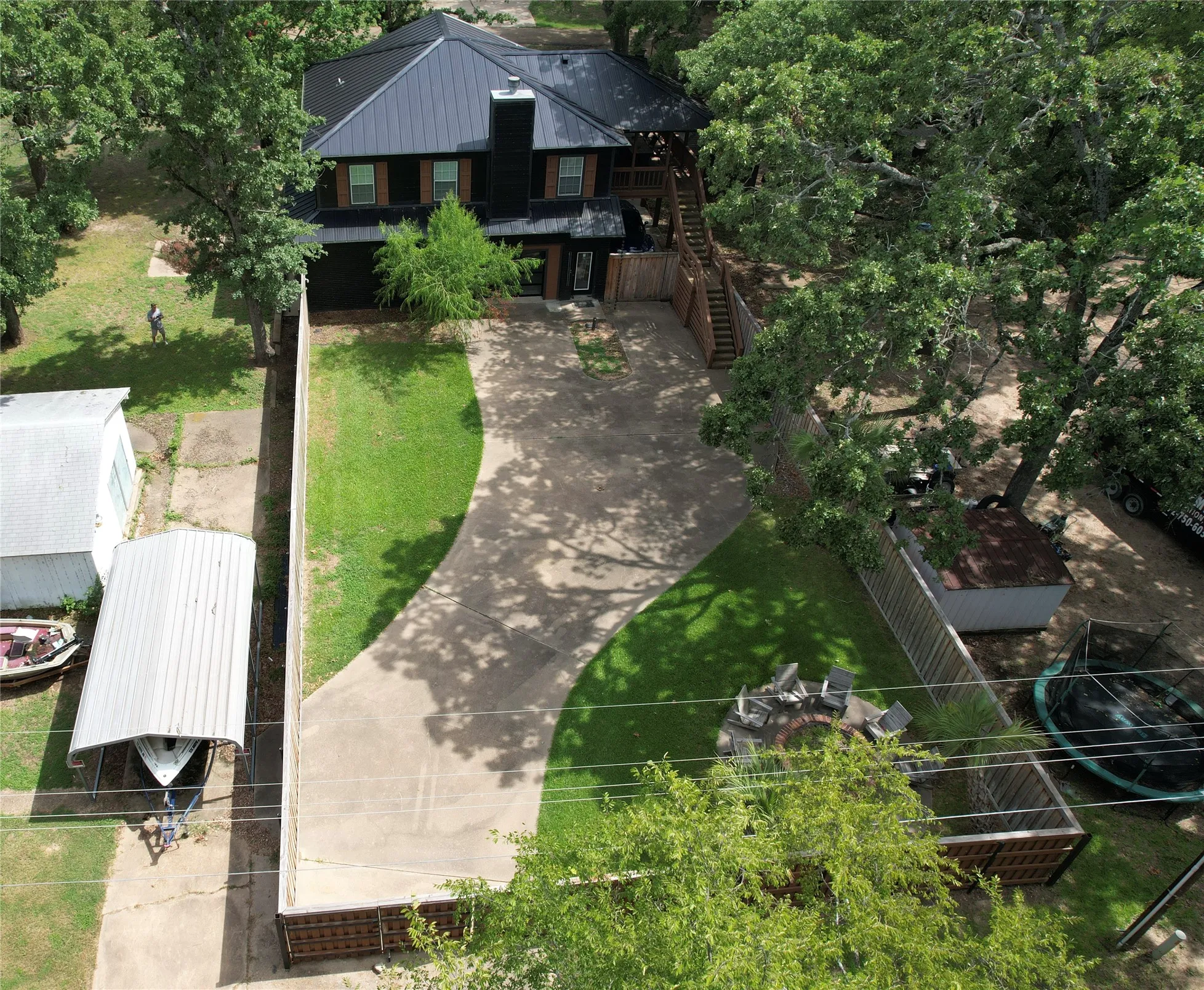Great aerial view of the White Oak Drive side of home with the private backyard, concrete driveway, grass yard with fire pit and the standing seam metal roof on house.