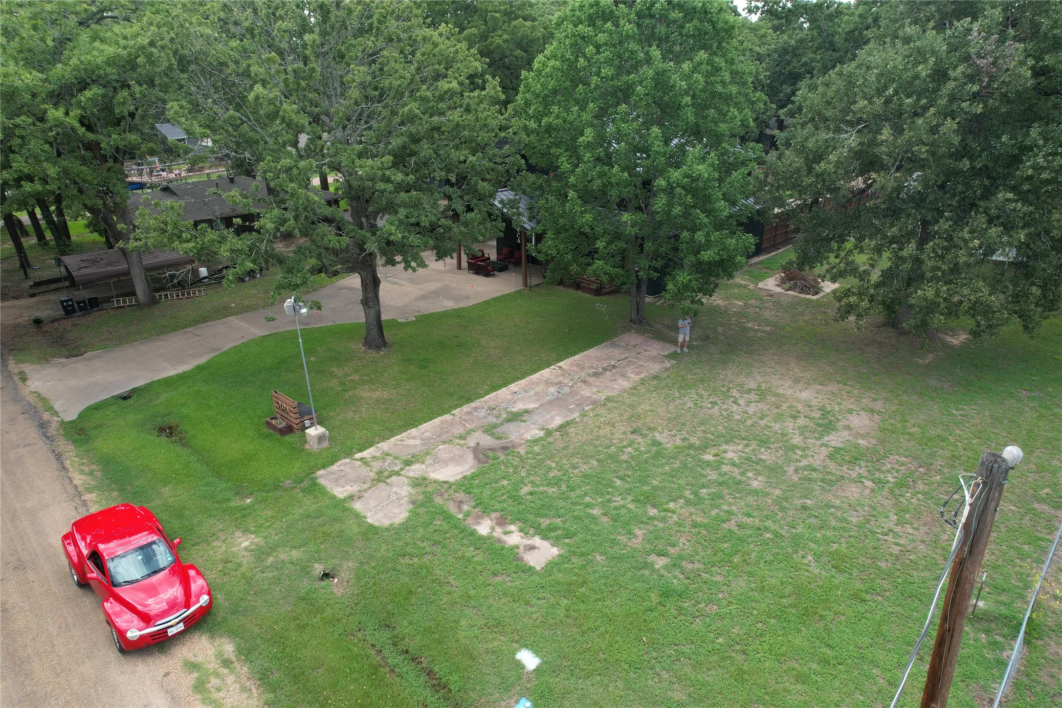 Adjacent grassy lot and a paved driveway are part of the property.  House is under a canopy of trees in the upper left corner of photo.