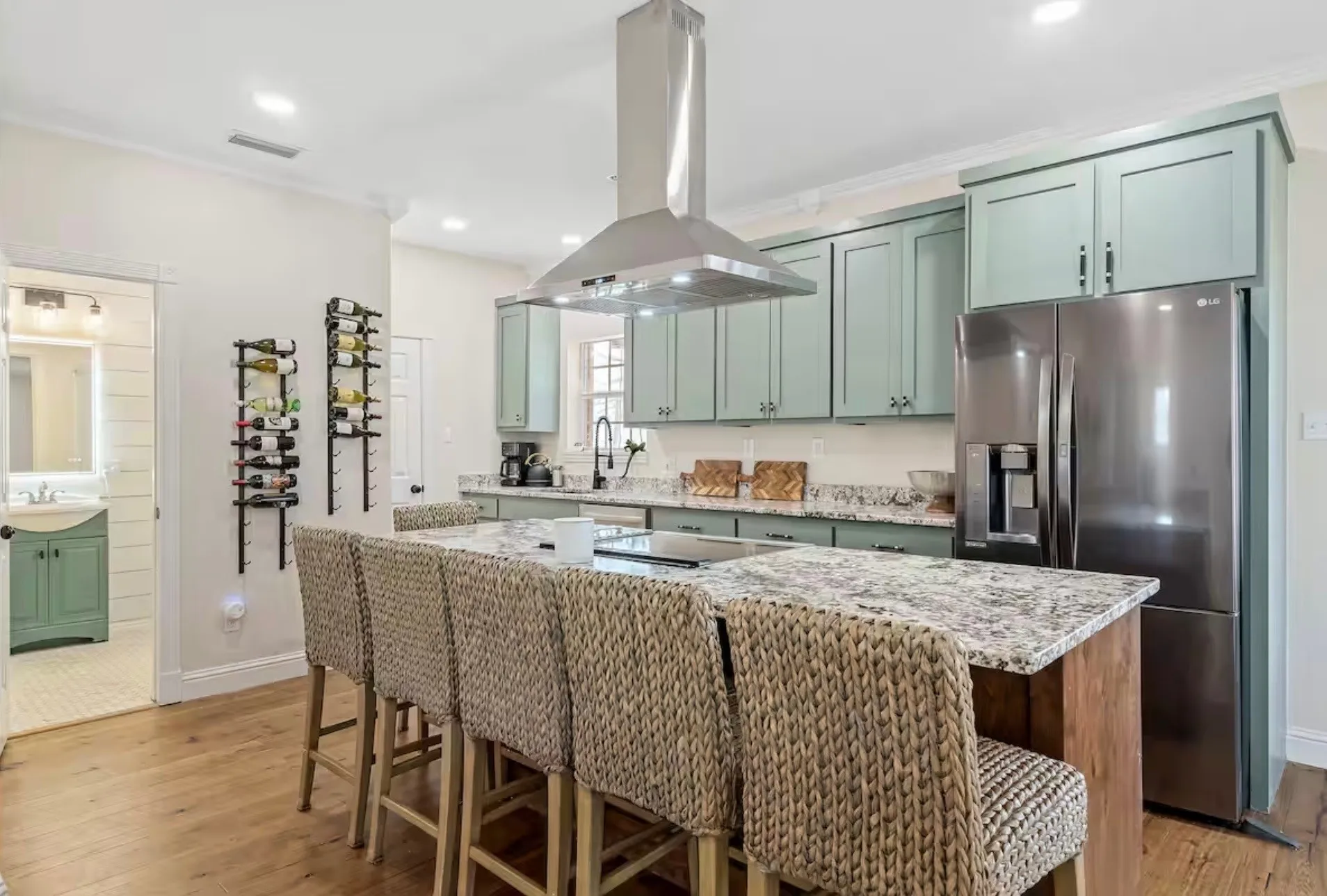 Kitchen featuring a central island with a stone countertop, light green cabinetry, stainless steel appliances, and wood-finish flooring