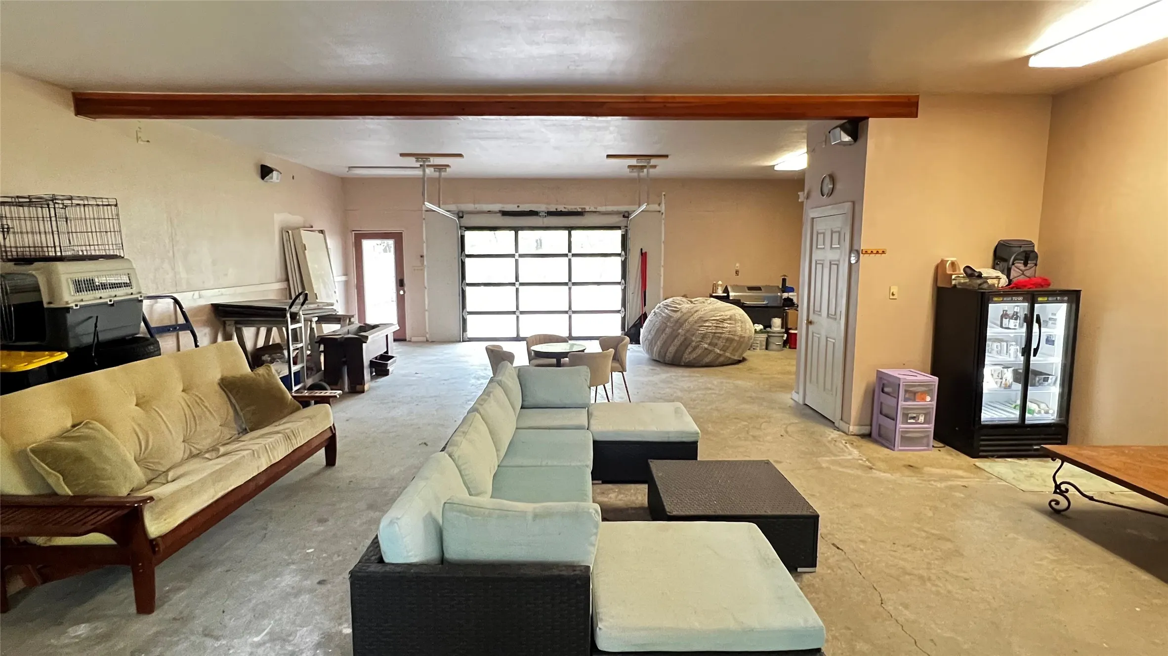 Barndo garage flex space finished out with a glass pane roll-up garage door letting the outdoor natural light in, wood beam, storage closet.