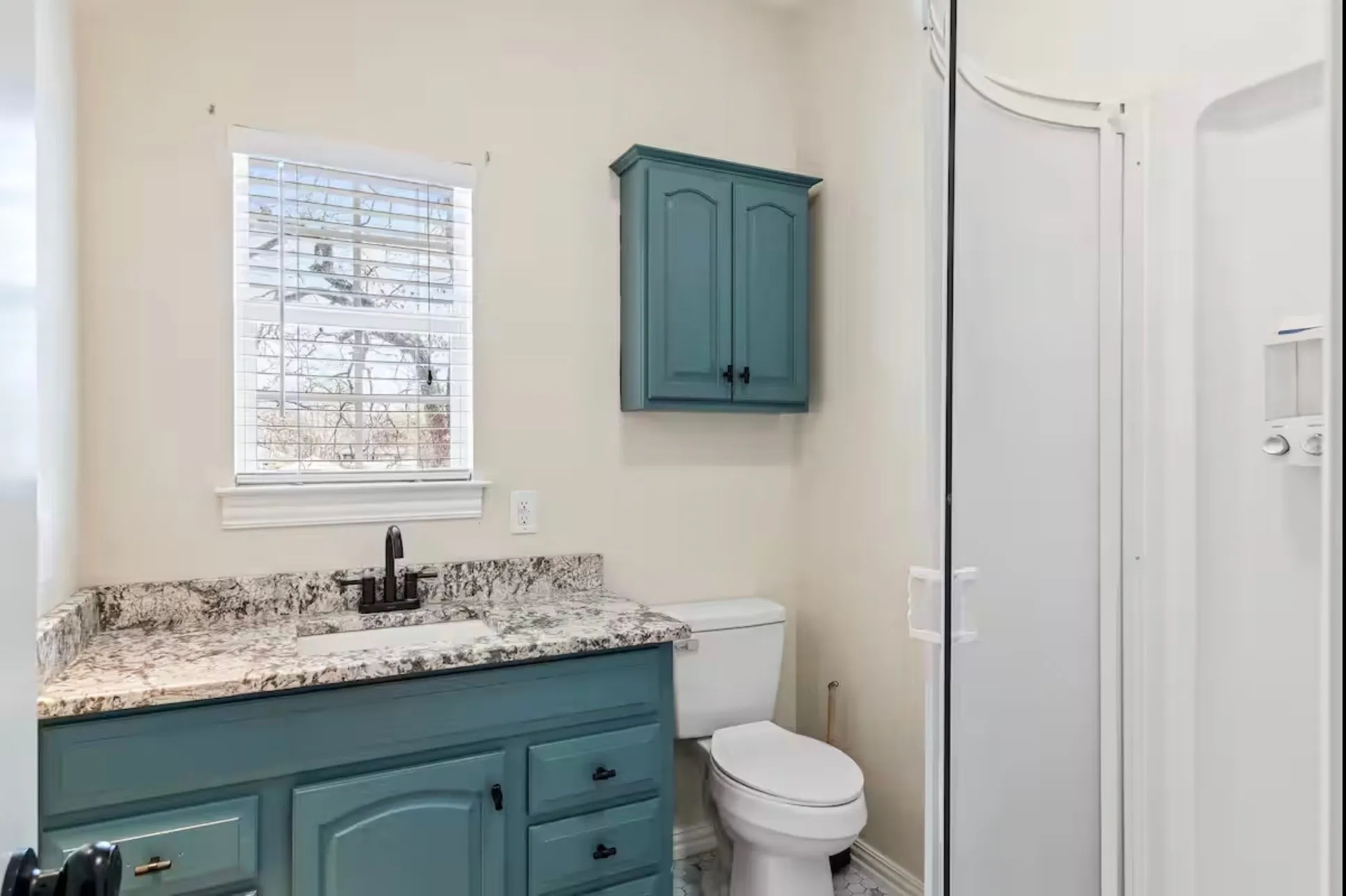 Bathroom 1 - with a single basin vanity featuring a stone countertop, teal cabinetry, and a black faucet