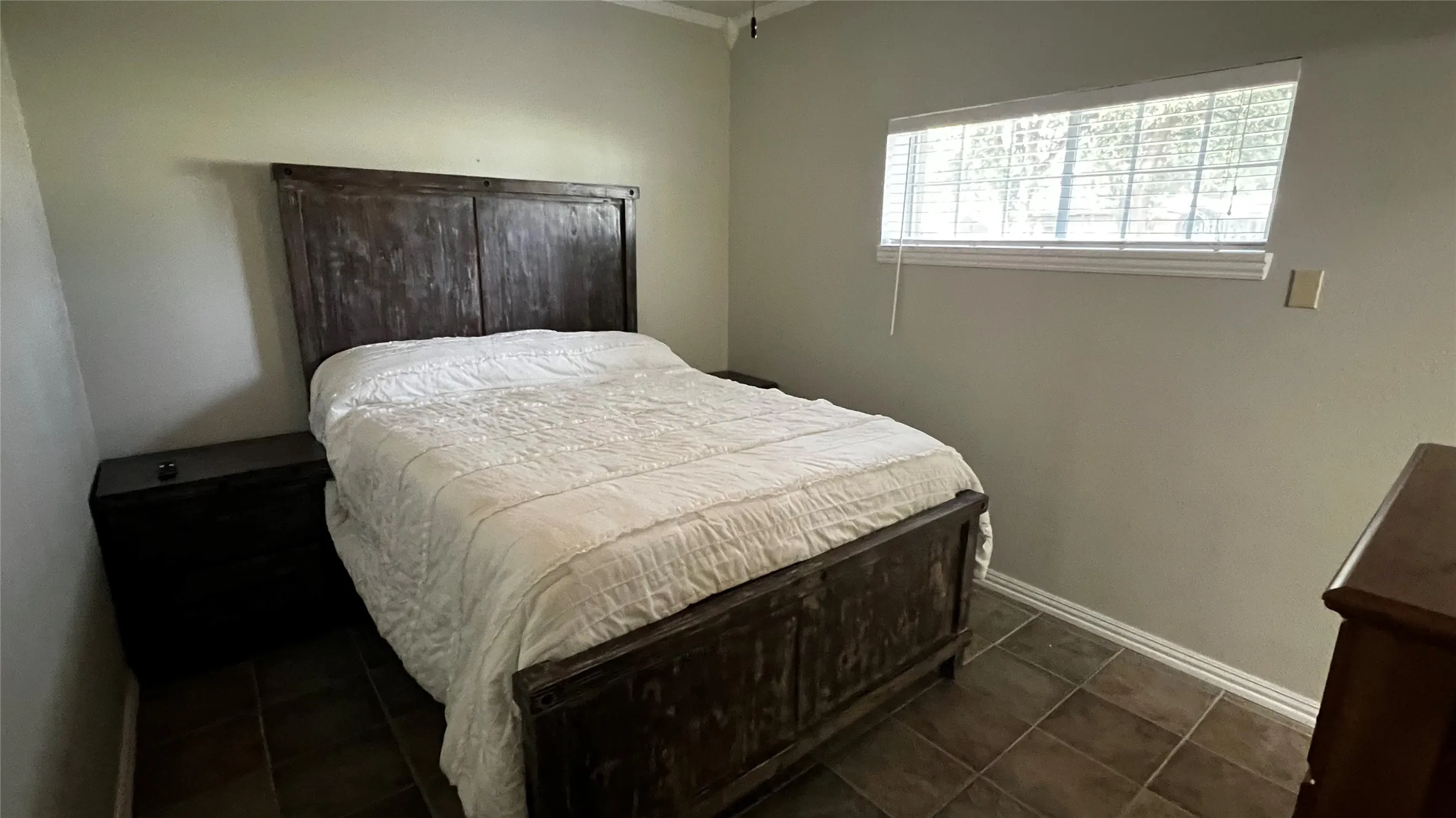 Primary Bedroom, located downstairs, featuring tile flooring, a horizontal window with blinds, and light-toned walls