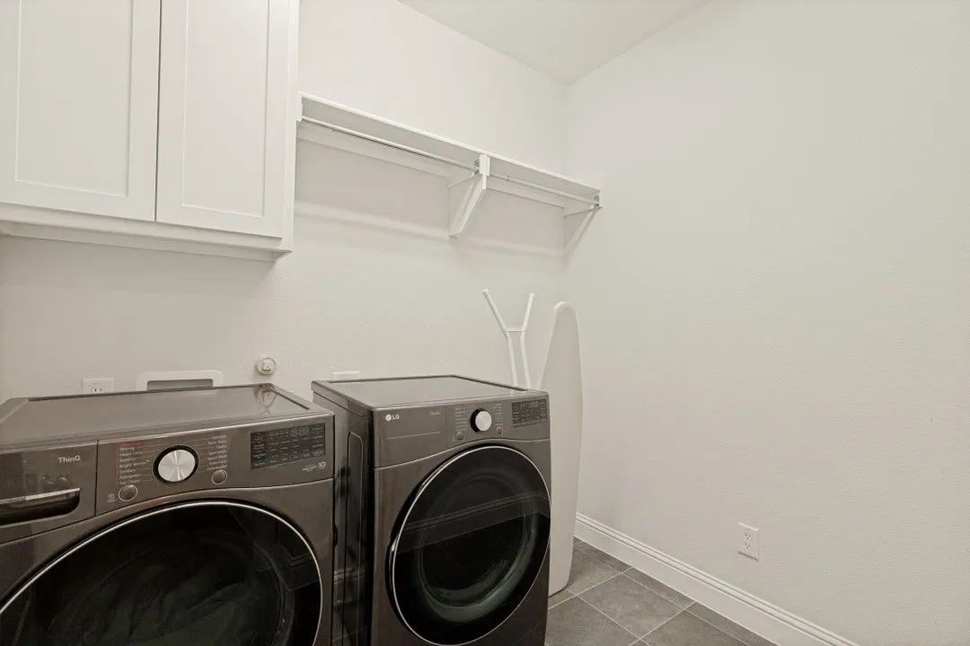 Dedicated laundry area featuring white upper cabinetry, a built-in wire shelf with hanging rod, and grey tile flooring