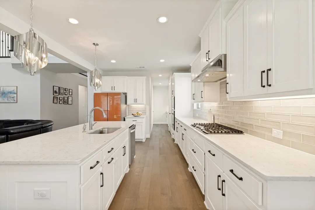 Open-concept kitchen featuring white cabinetry, light-toned countertops, a gas cooktop with a stainless steel range hood, and wood-finish flooring
