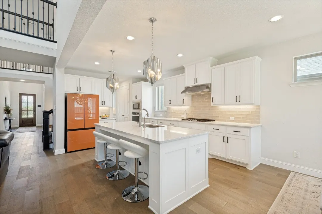 Gourmet kitchen with a large central island, white shaker cabinetry, quartz countertops, subway tile backsplash, and wood-finish flooring
