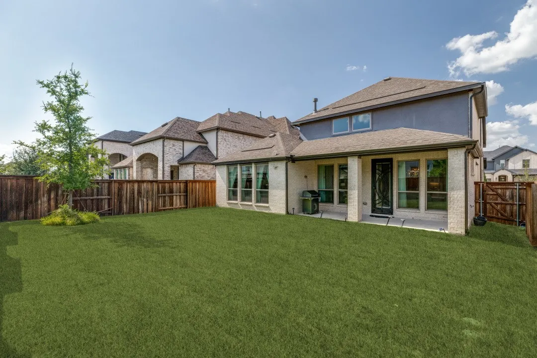 Expansive backyard with a manicured lawn, full privacy fencing, and a covered patio