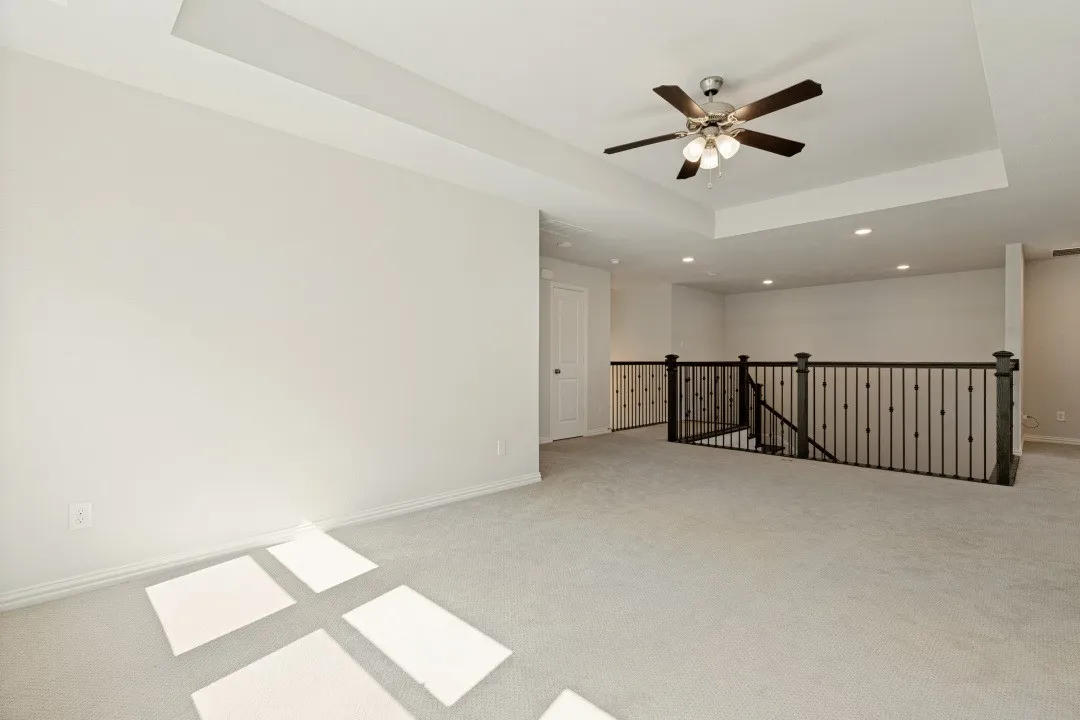 Expansive carpeted area featuring a tray ceiling with a ceiling fan
