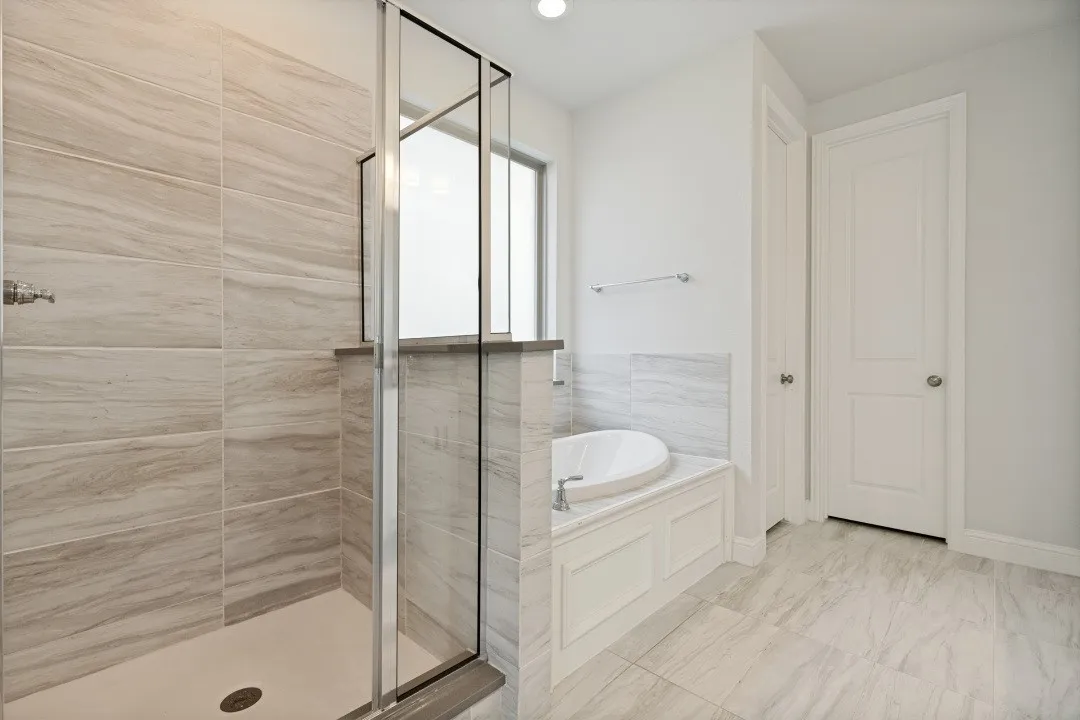 Modern bathroom featuring a tiled shower with glass enclosure, a built-in soaking tub with paneling, and large format floor tiles