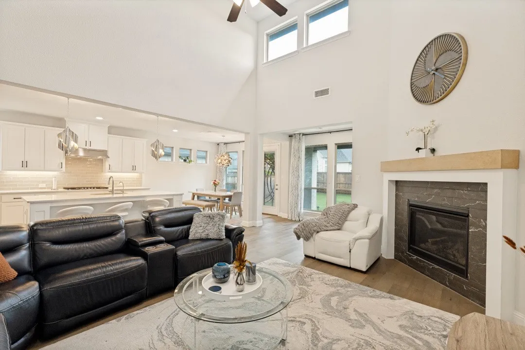Open-concept living area featuring a vaulted ceiling with a fan, wood-finish flooring, and a fireplace with a stone surround and wood mantel