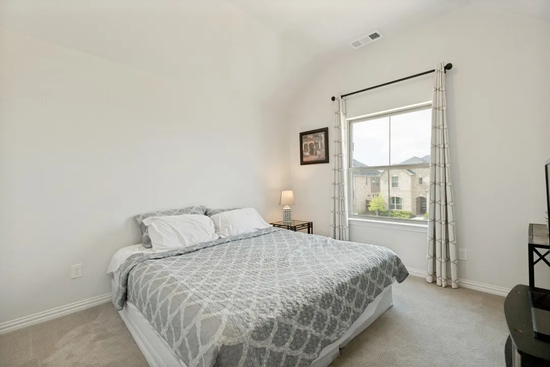 Vaulted ceiling bedroom featuring a large window with white trim, light-toned carpeting, and white baseboards
