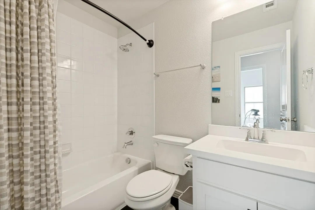 Bathroom featuring a white vanity with a built-in sink, chrome fixtures, and a white tile shower surround over a tub