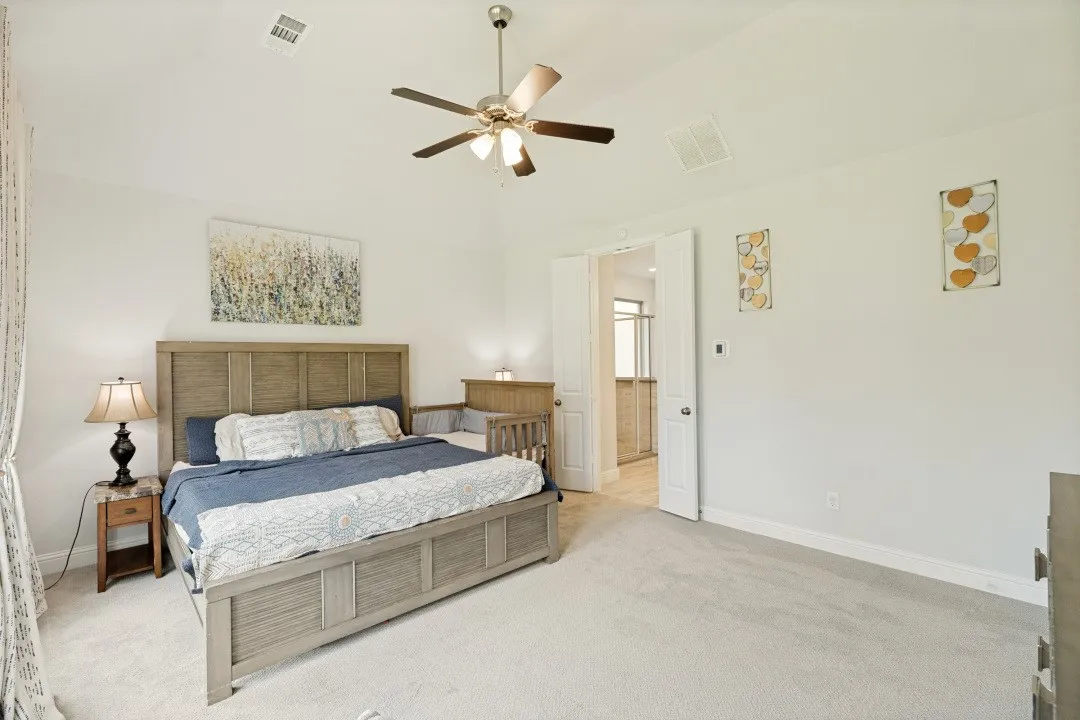 Carpeted bedroom featuring vaulted ceilings, a ceiling fan with integrated lighting, and direct access to an en-suite bathroom