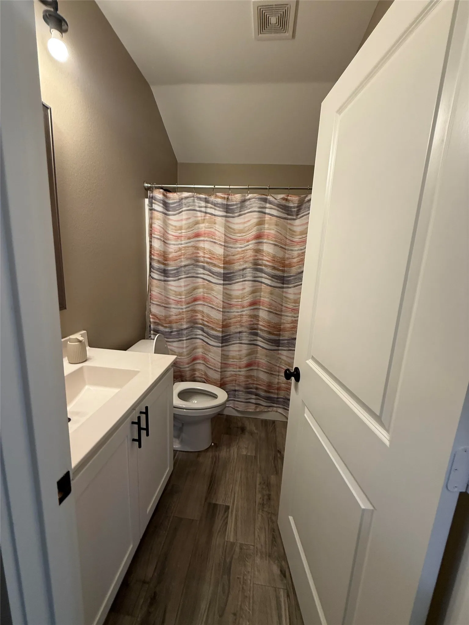 Bathroom featuring a white vanity with integrated sink, dark hardware, wood-finish flooring, and a shower area