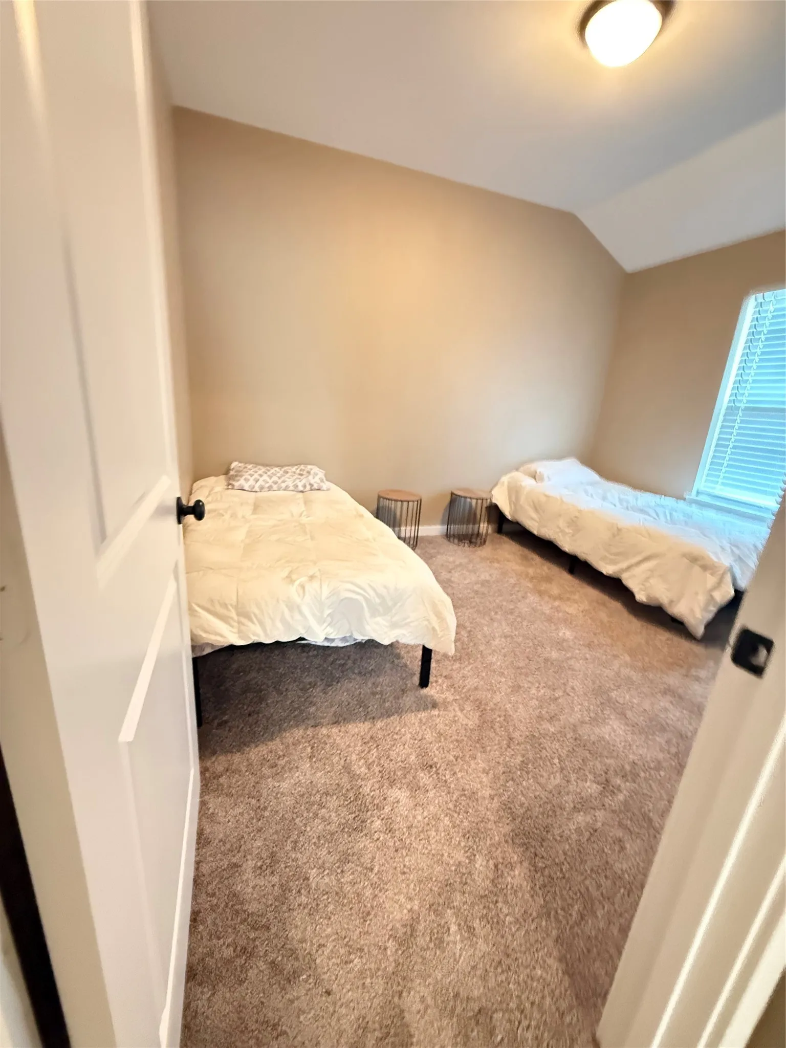 Carpeted room featuring a neutral color palette, a window with blinds, and a ceiling-mounted light fixture